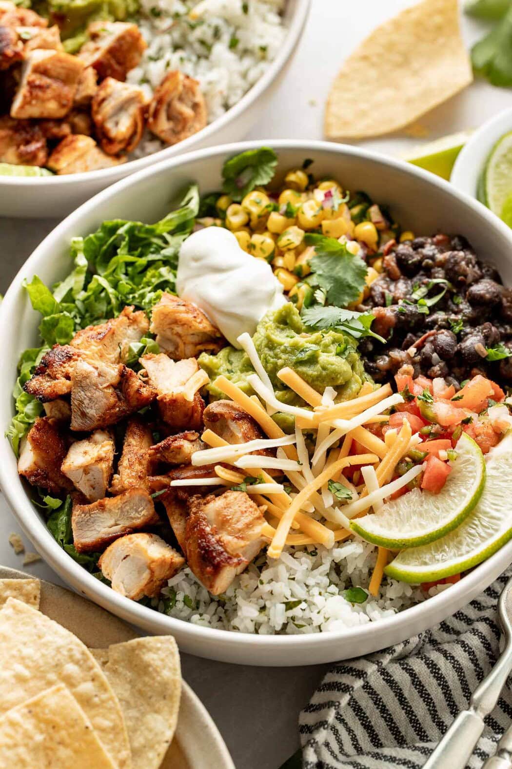 Close up view of a chipotle chicken bowl filled with rice, beans, corn salsa and garnished with lime wedges.