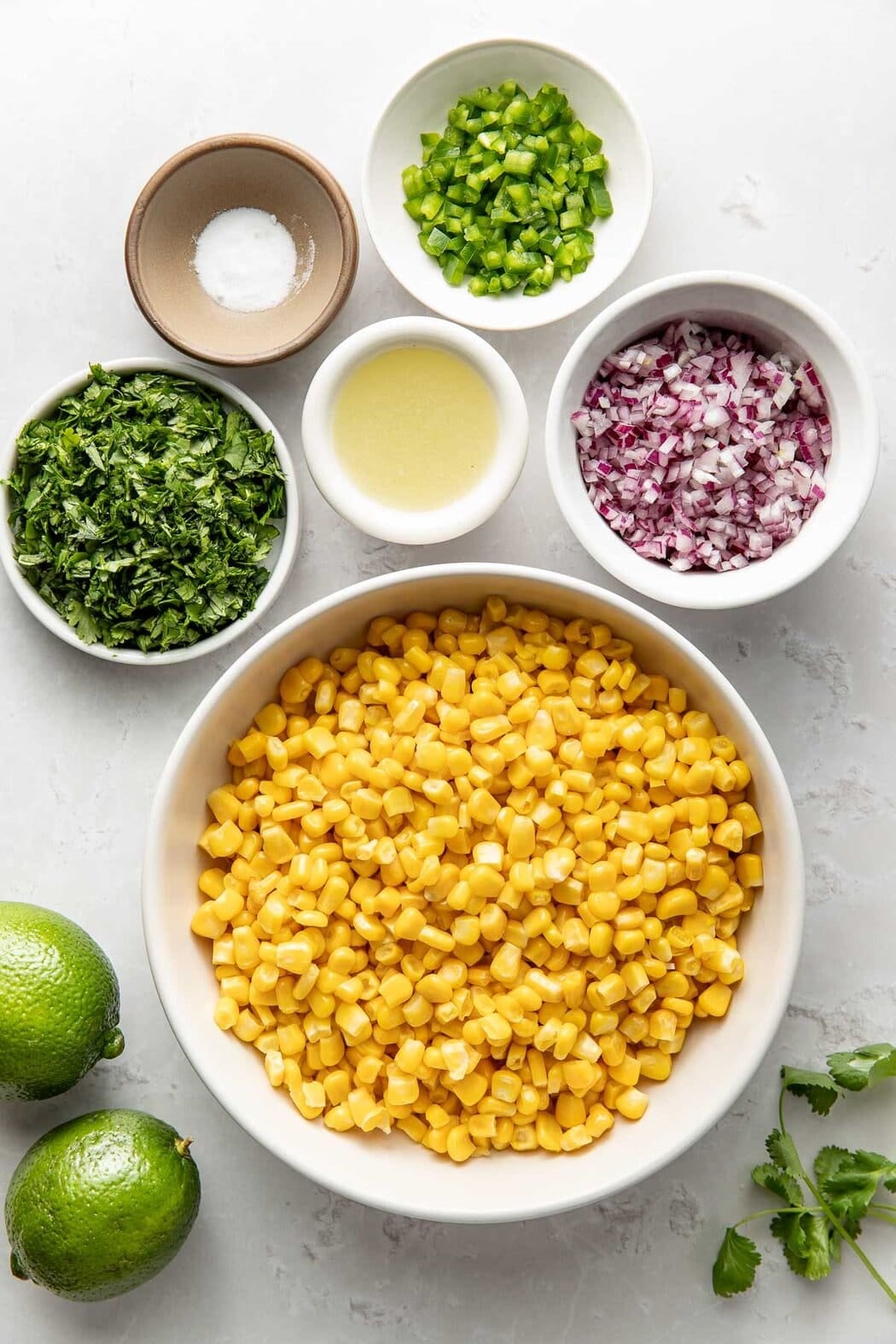 Overhead view of a variety of ingredients for Copycat Chipotle Corn Salsa in different sized bowls. 