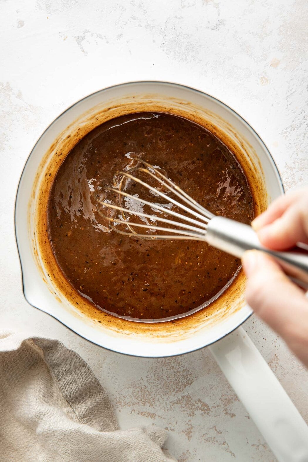 Overhead view of a saucepan filled with a ham glaze being whisked with a metal whisk.