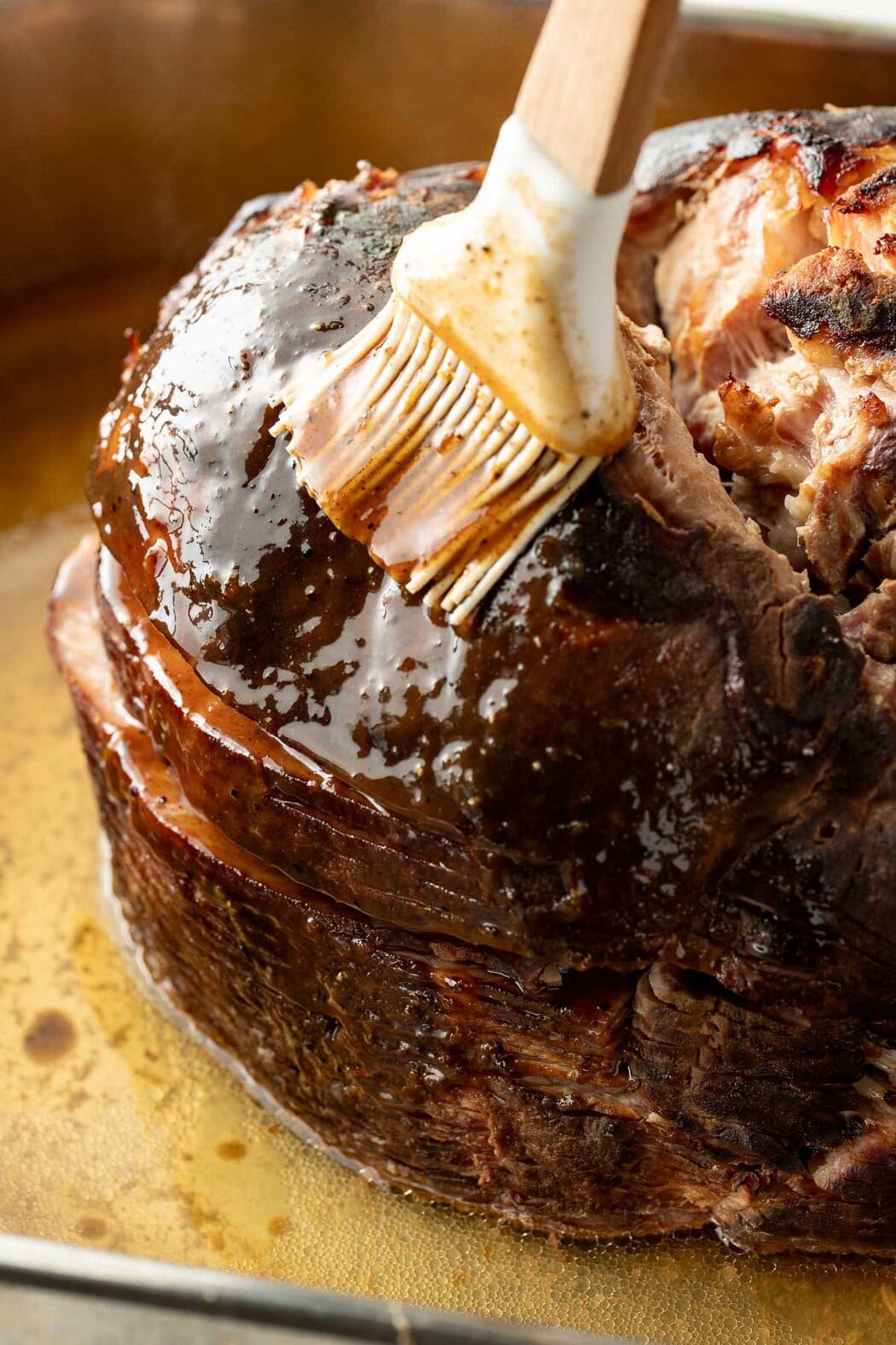 Close up view of a large ham being coated with a ham glaze.