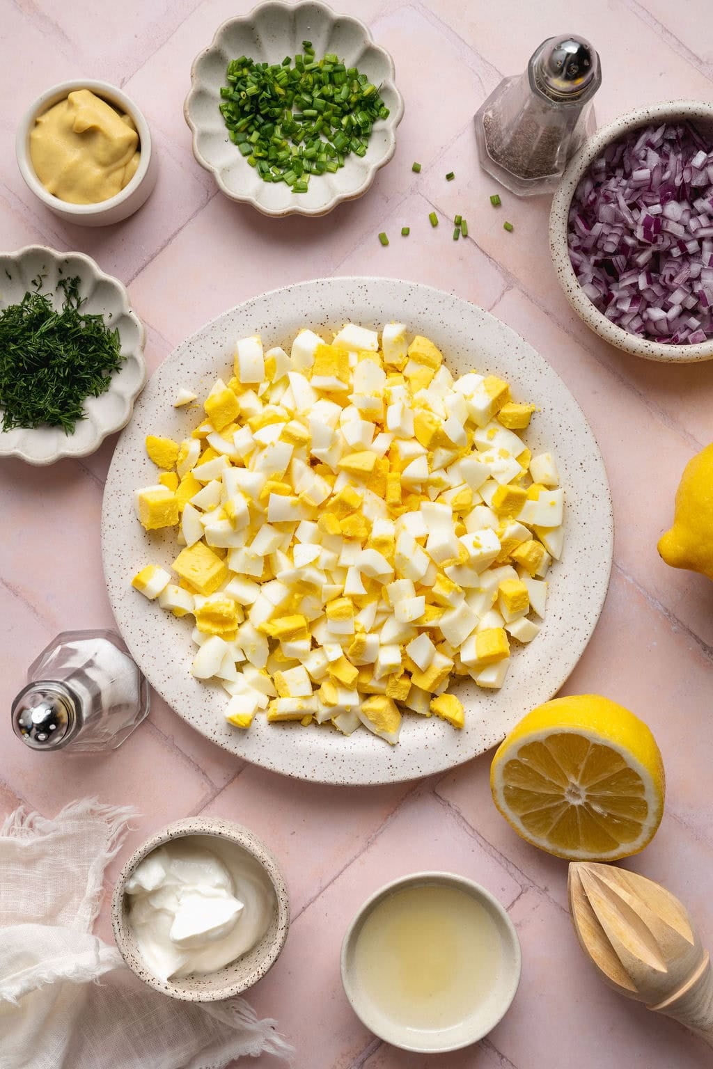 Overhead view of a variety of ingredients for egg salad in different sized bowls. 