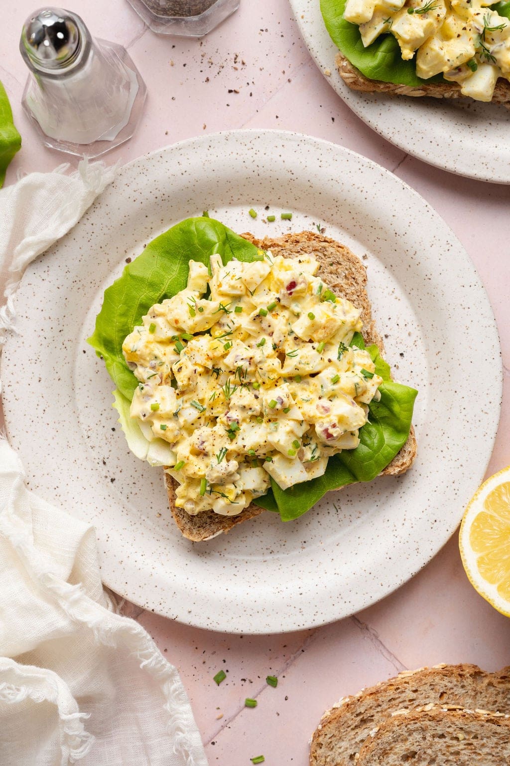 Overhead view of a plate of an open-faced egg salad sandwich topped with fresh chives and dill. 