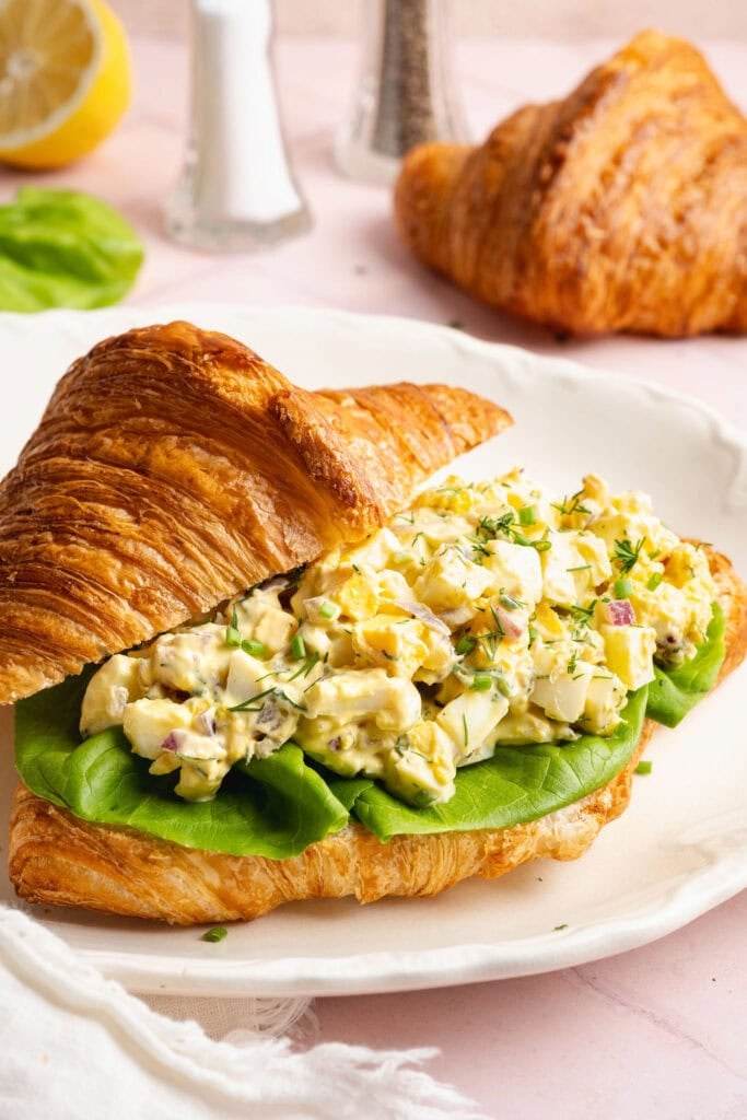 Close up view of a croissant filled with egg salad and lettuce. 