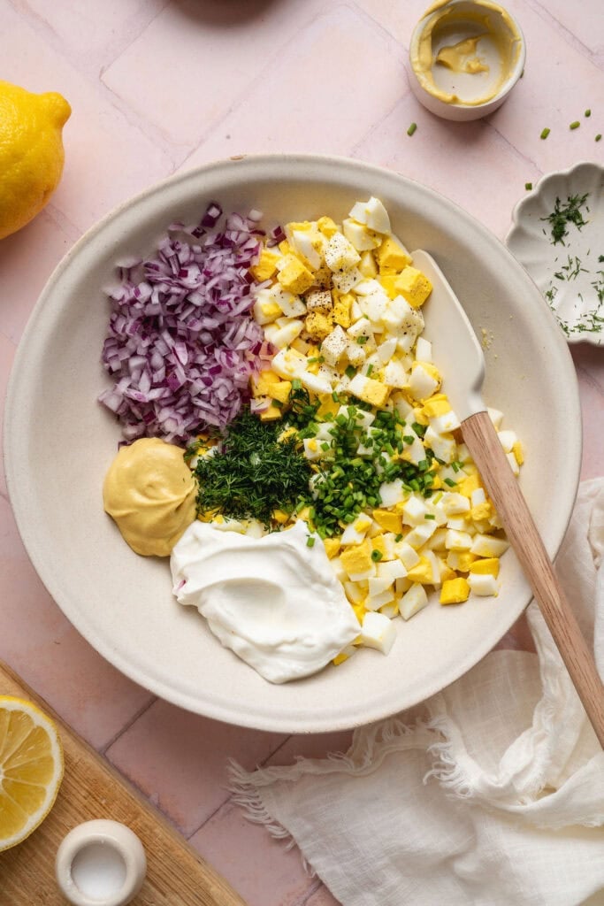 Overhead view of a bowl of egg salad ingredients ready to be stirred. 