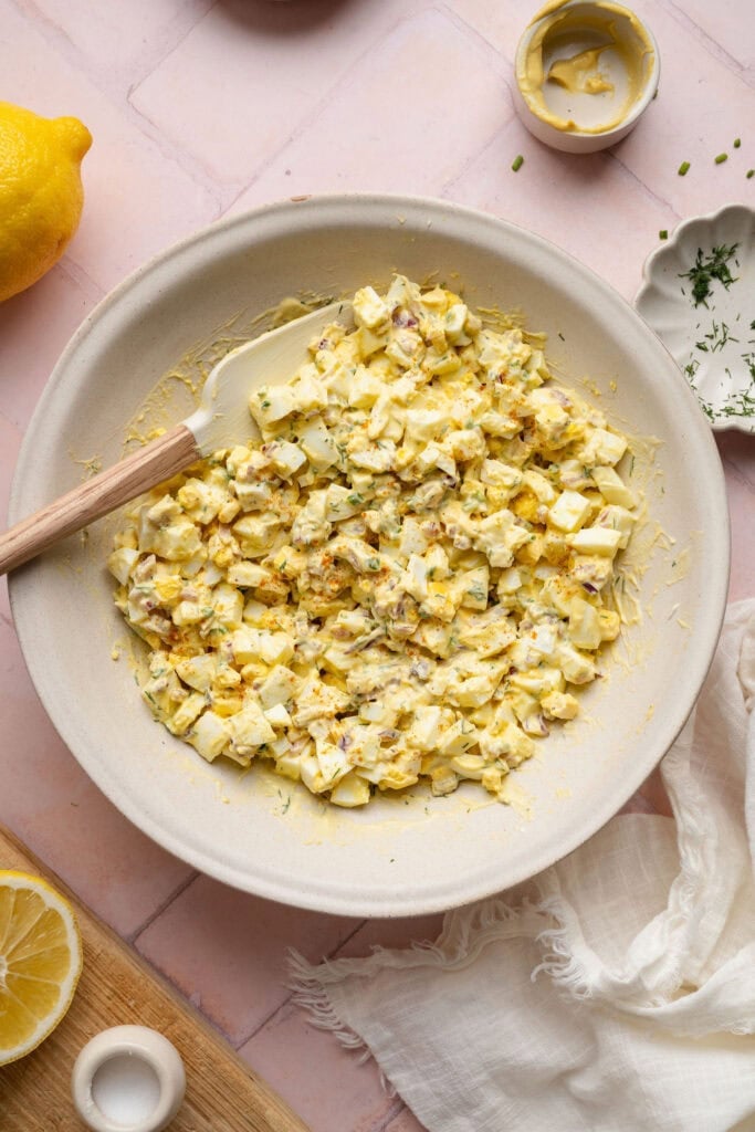 Overhead view of a bowl of egg salad with a spatula stuck in the side. 