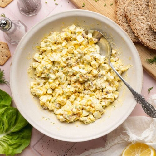 Overhead view of a bowl of egg salad topped with fresh chives and dill.