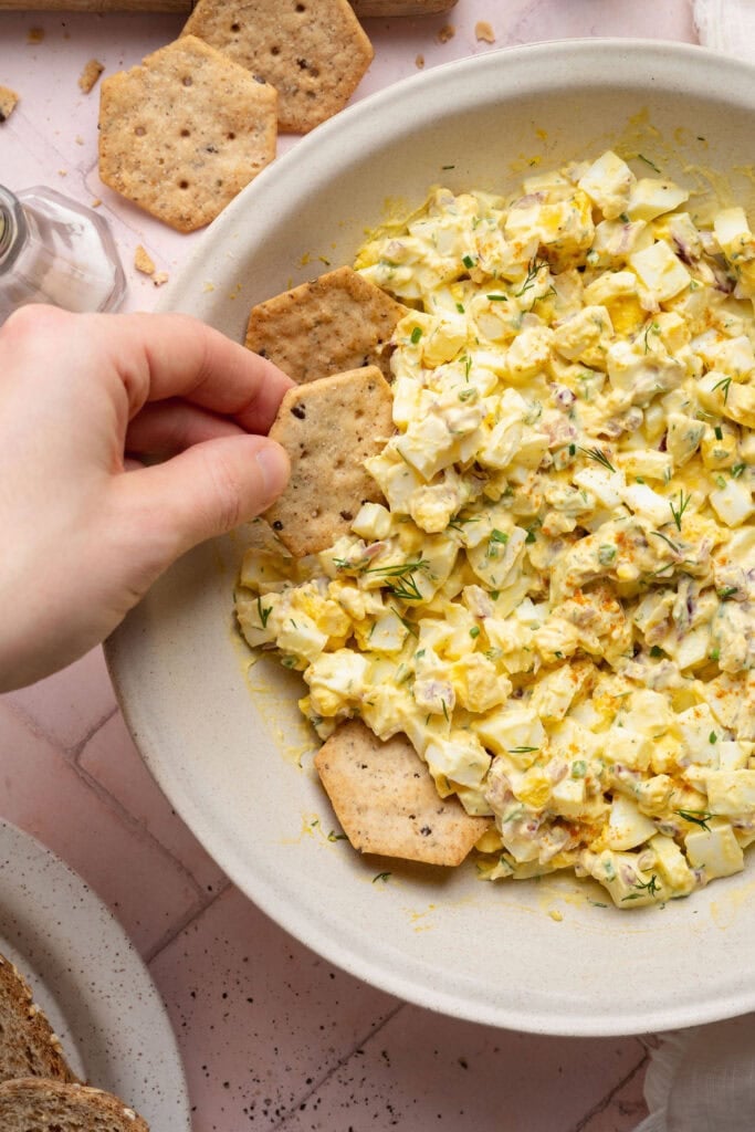 Overhead view of a bowl of egg salad with crackers on the side. 