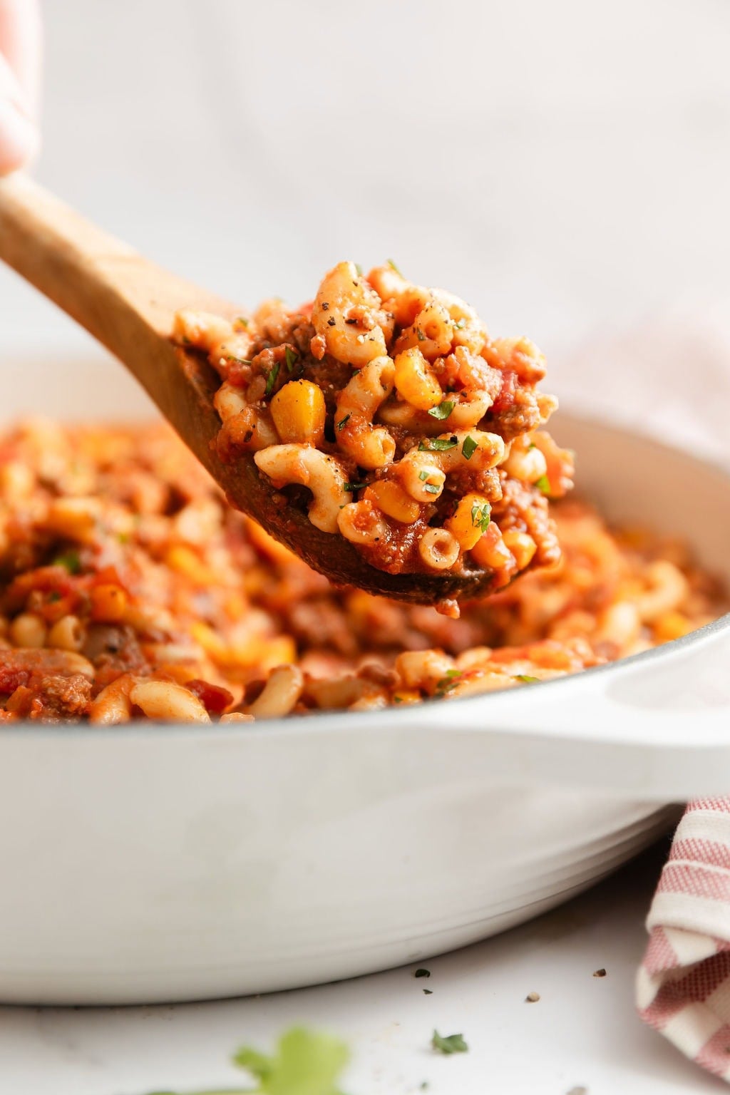 Close up view of a wooden spoon scooping out a spoonful of goulash from a skillet.