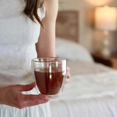 Close up view of a women holding a glass mug of nighttime tea in a bedroom.
