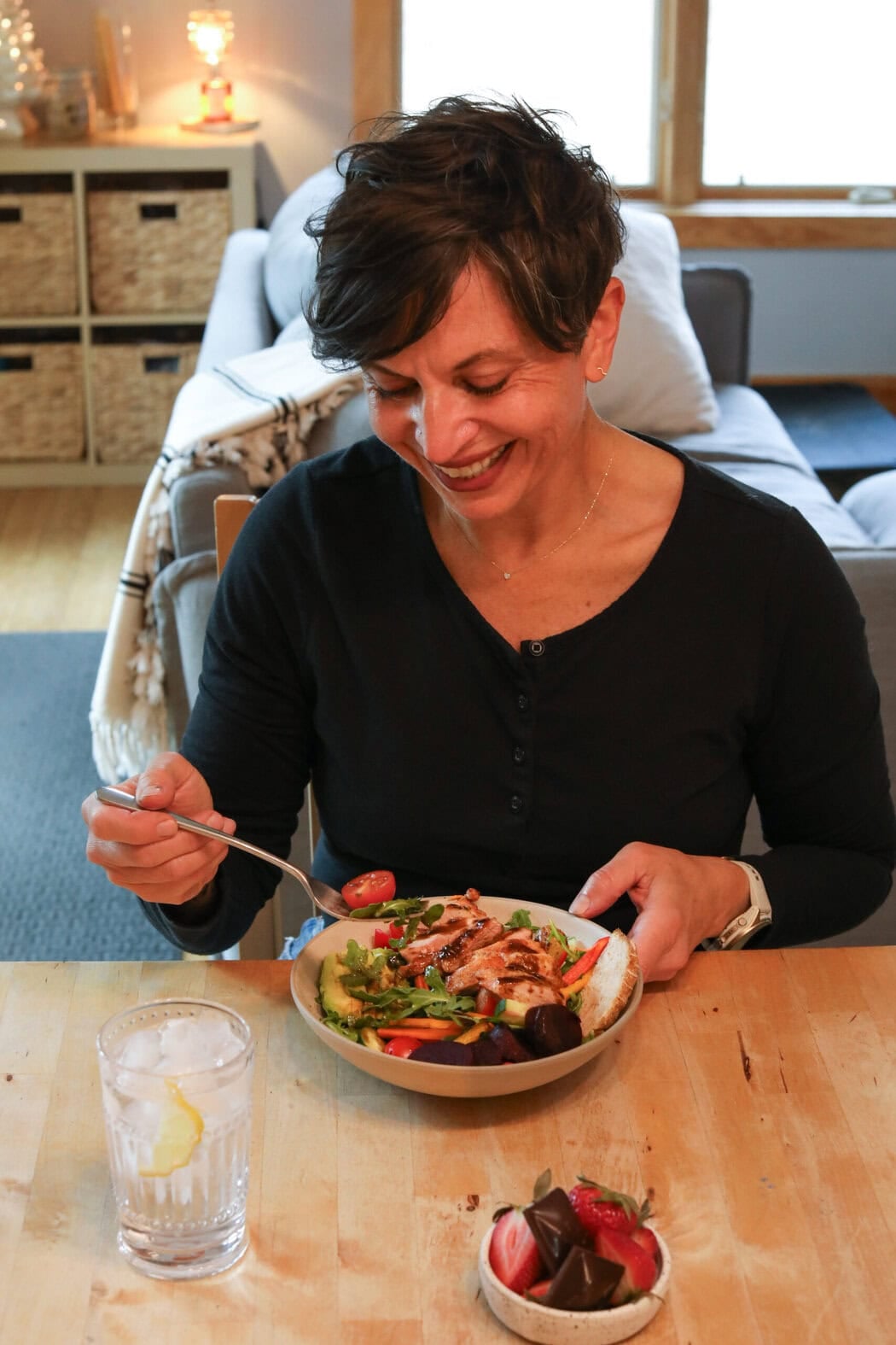 Close up view of a woman sitting at a table eating a bowl of salad with grilled chicken on top. 