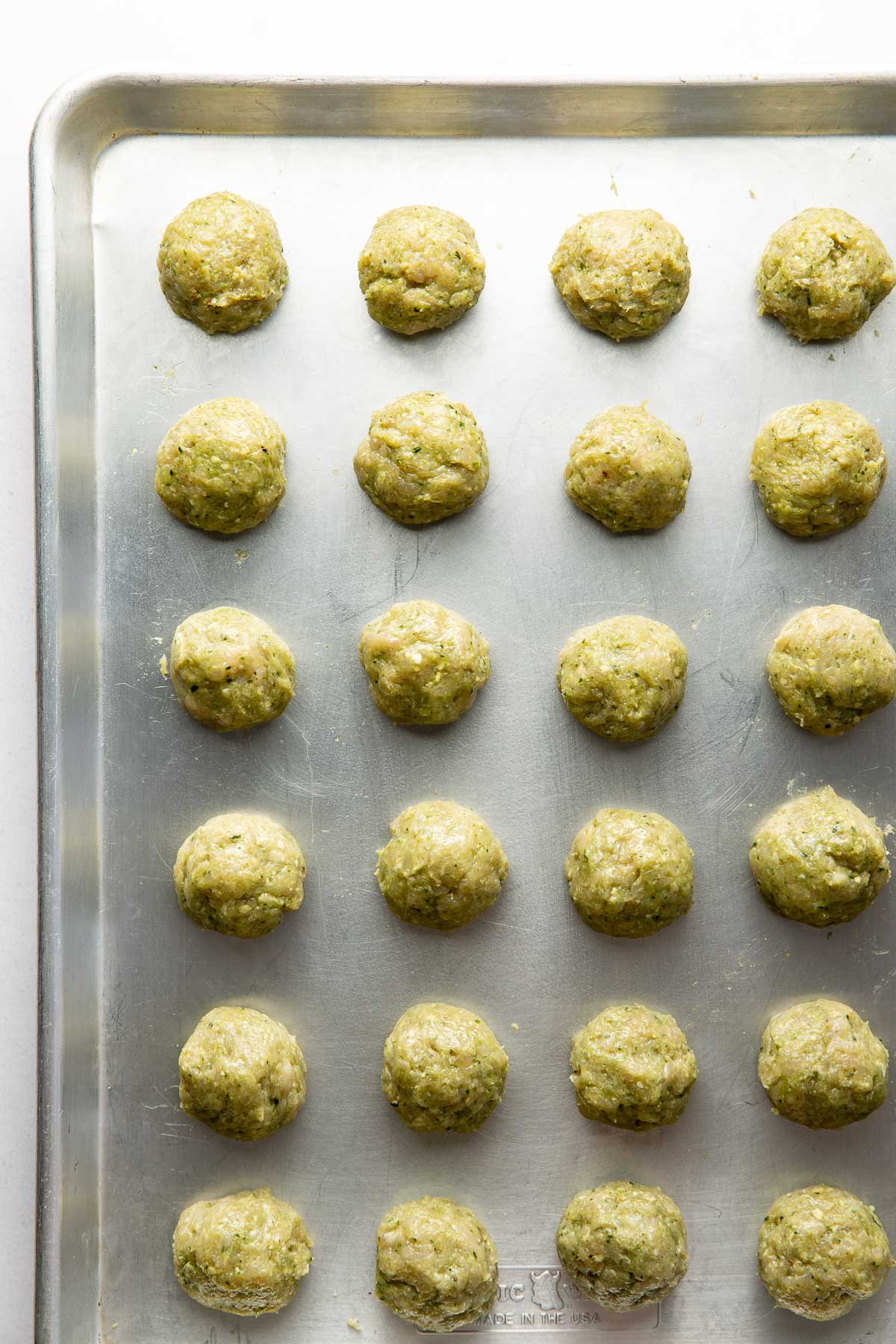 Overhead view of a sheet pan filled with Pesto Meatballs ready for baking. 