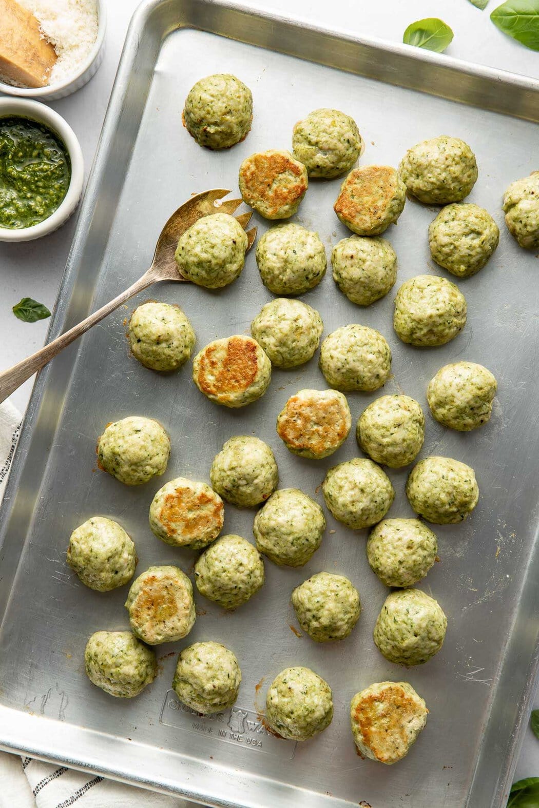 Overhead view of a sheet pan of freshly baked Pesto Meatballs showing the browned bottoms. 