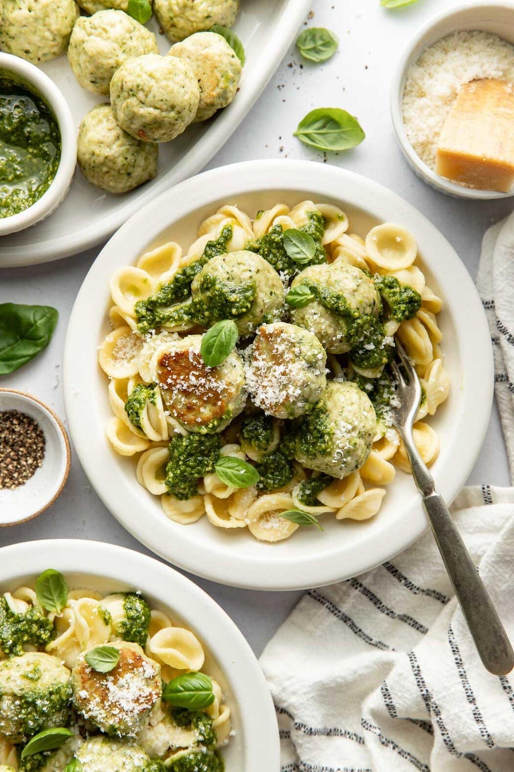 Overhead view of a plate of pasta topped with Pesto Meatballs sprinkled with parmesan cheese and fresh basil. 