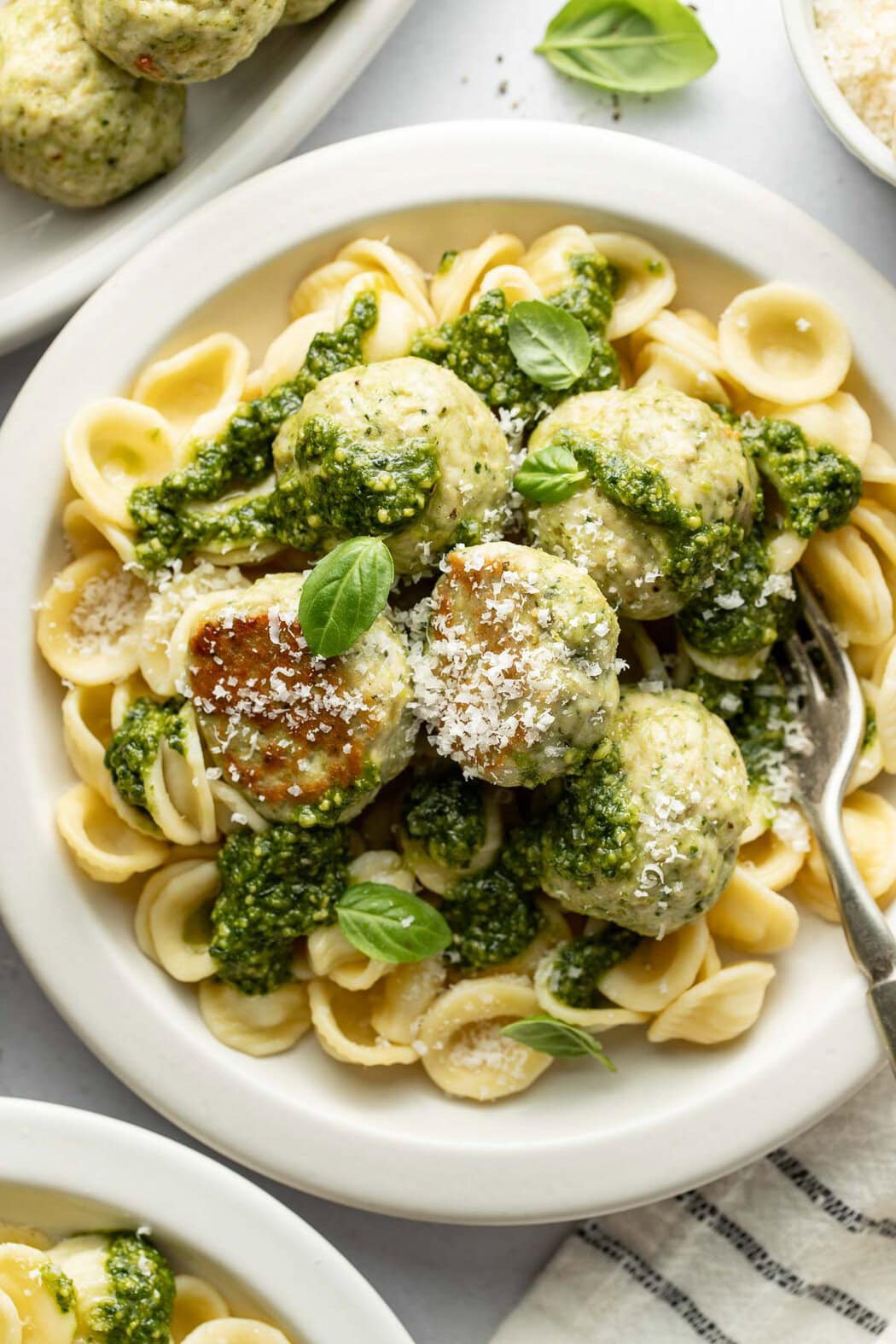 Overhead view of a plate of pasta topped with Pesto Meatballs sprinkled with parmesan cheese and fresh basil. 