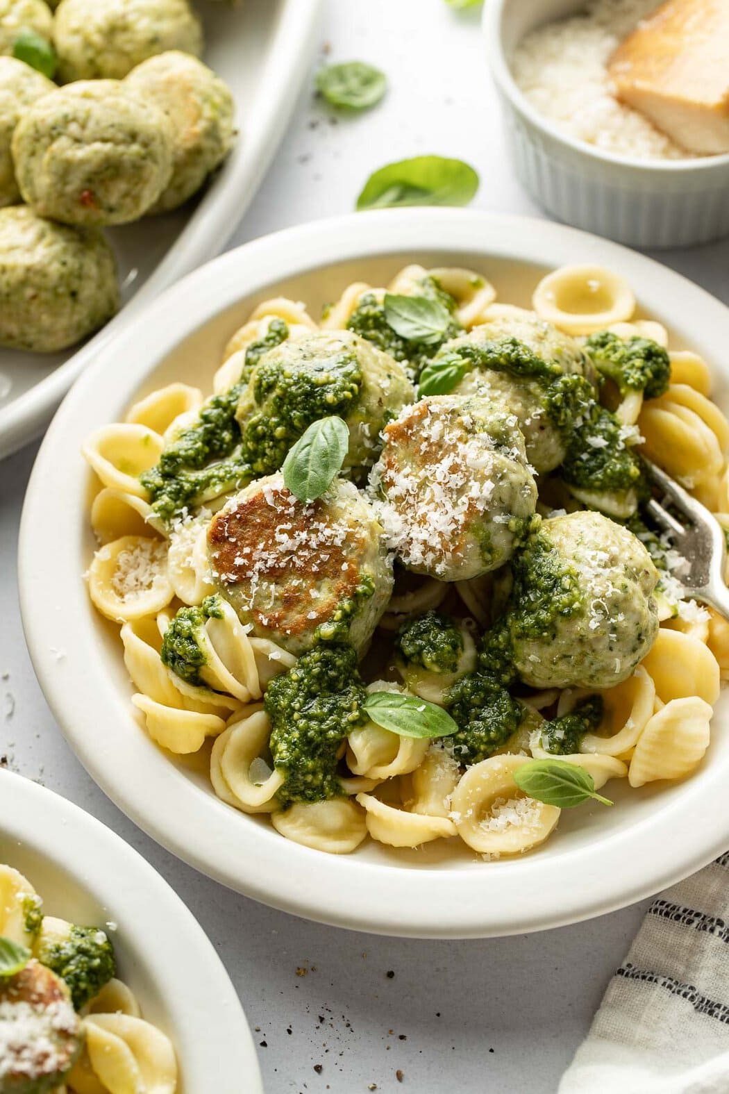 Close up view of a plate of pasta topped with Pesto Meatballs sprinkled with parmesan cheese and fresh basil. 