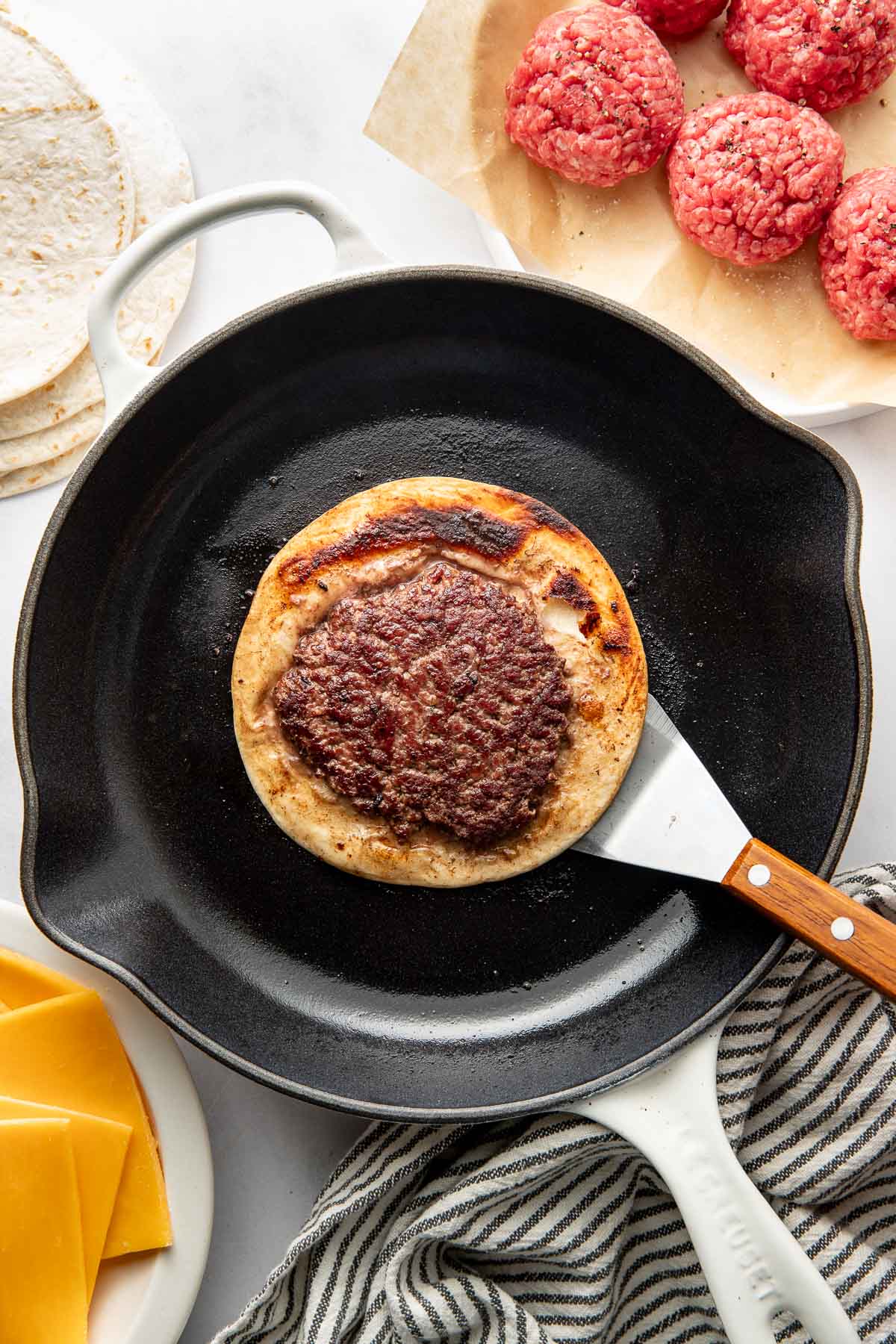 Overhead view of a fry pan with a spatula holding a Smash Burger Taco over it. 