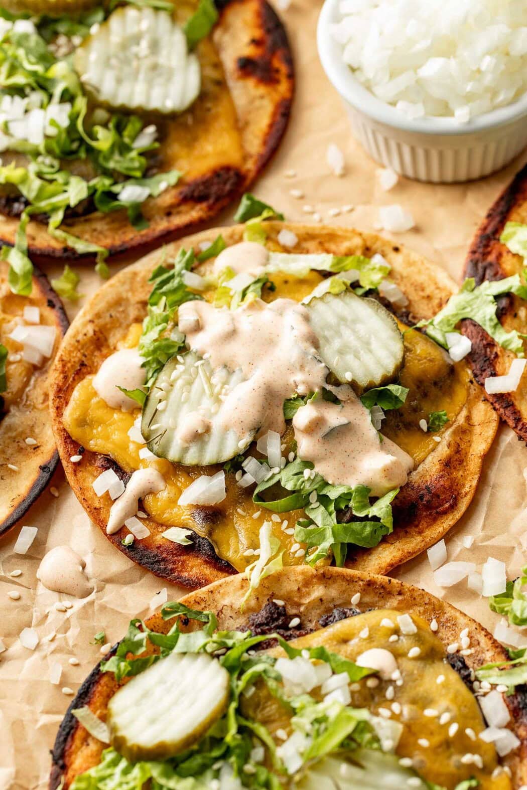 Close up view of Smash Burger Tacos on parchment paper topped with special sauce and pickles. 