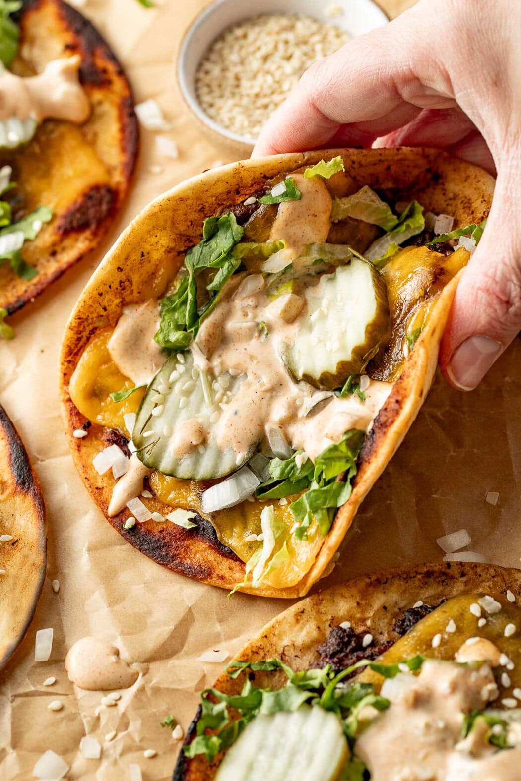 Close up view of a hand grabbing a Smash Burger Taco topped with special sauce and pickles.