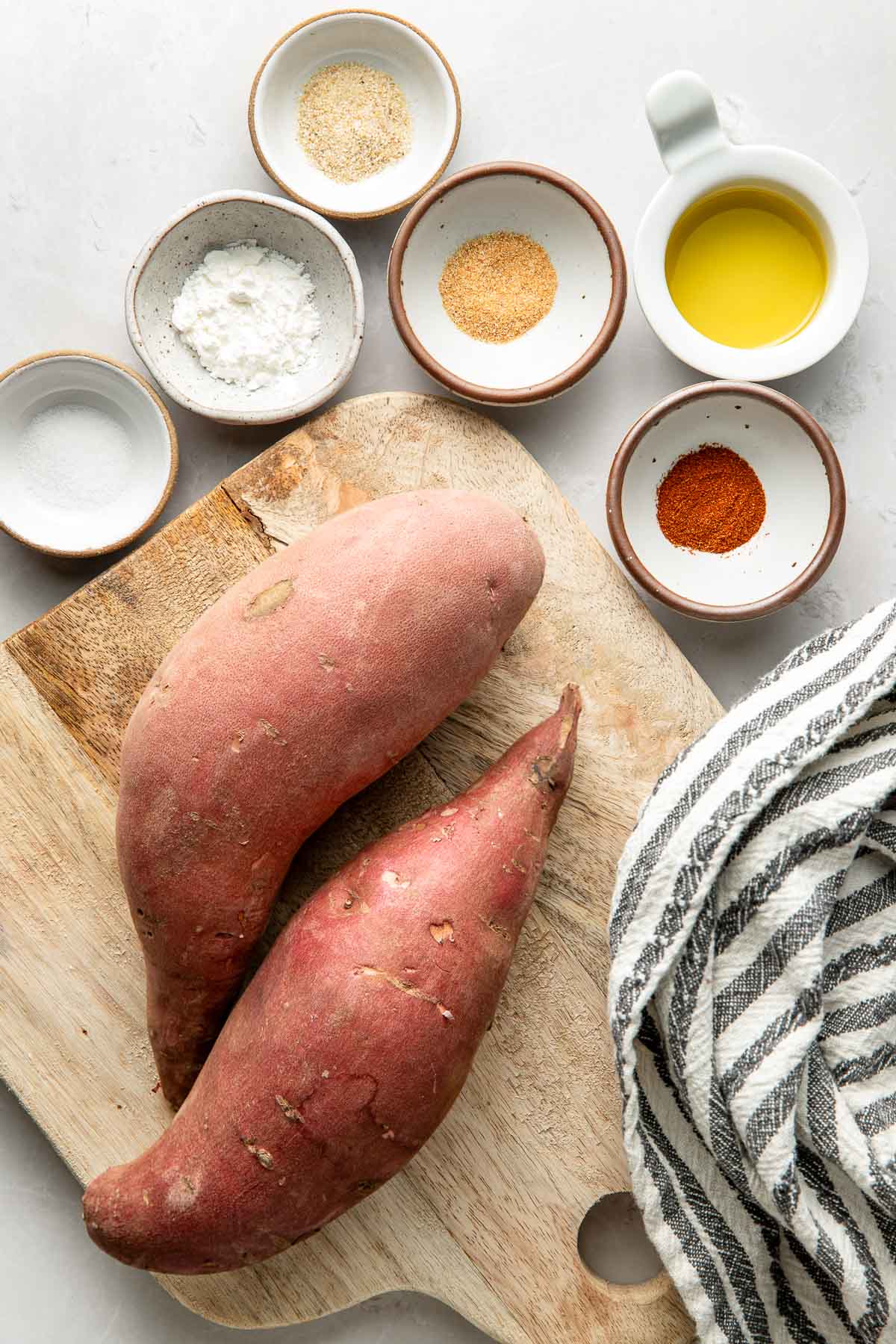 Overhead view of a variety of ingredients for sweet potato fries arranged in different sized bowls.
