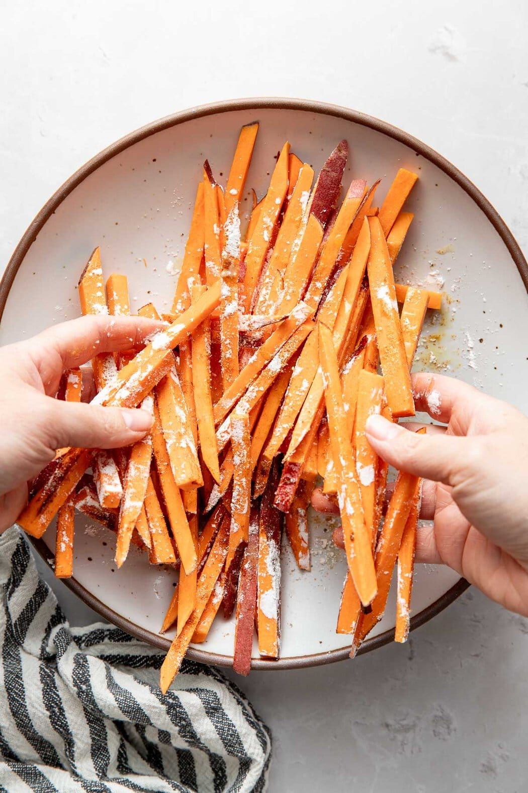 Overhead view of hands tossing sweet potato strips in seasonings and corn starch.