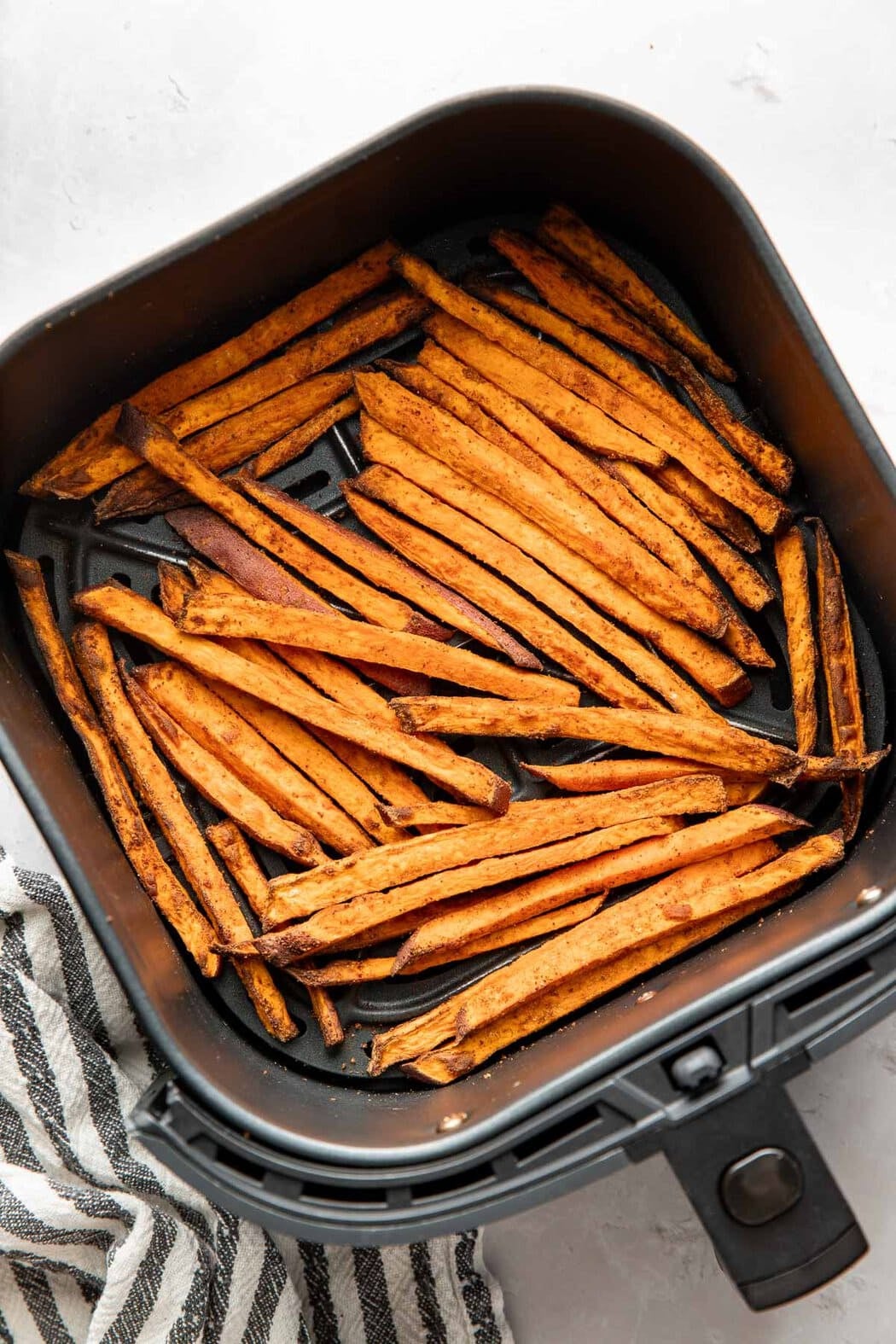 Overhead view of an air fryer basket filled with sweet potato fries.