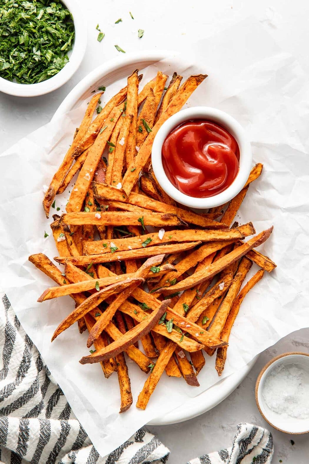 Overhead view of Air Fryer Sweet Potato Fries on parchment paper arranged around a small bowl of ketchup.