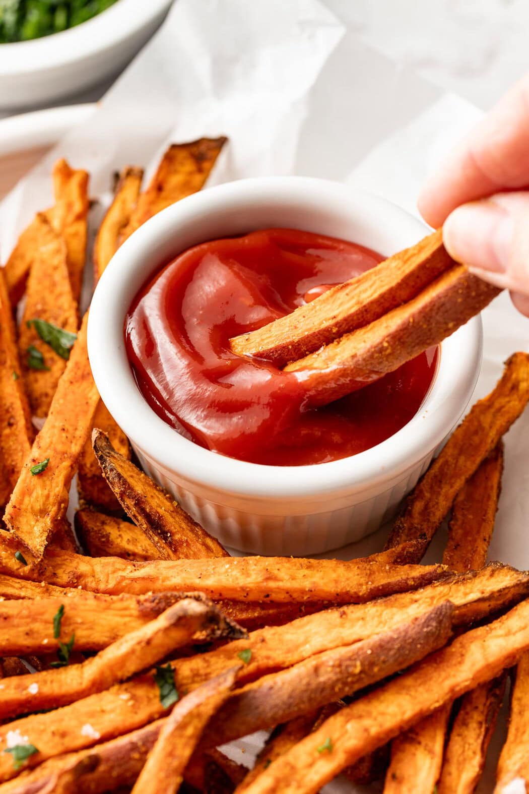 Close up view of a hand dipping two Air Fryer Sweet Potato Fries into ketchup.