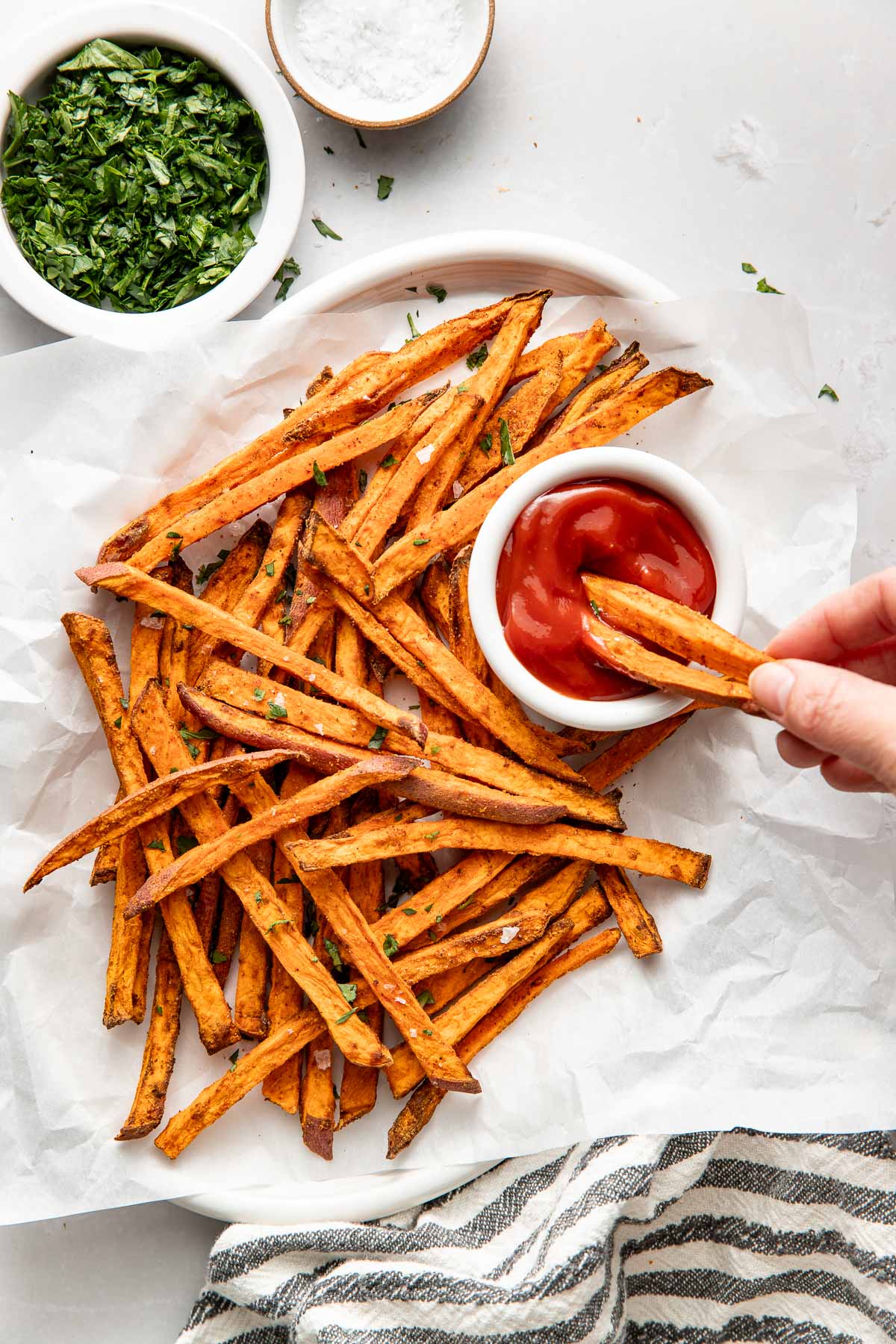 Overhead view of Air Fryer Sweet Potato Fries with a hand dipping two fries into ketchup.