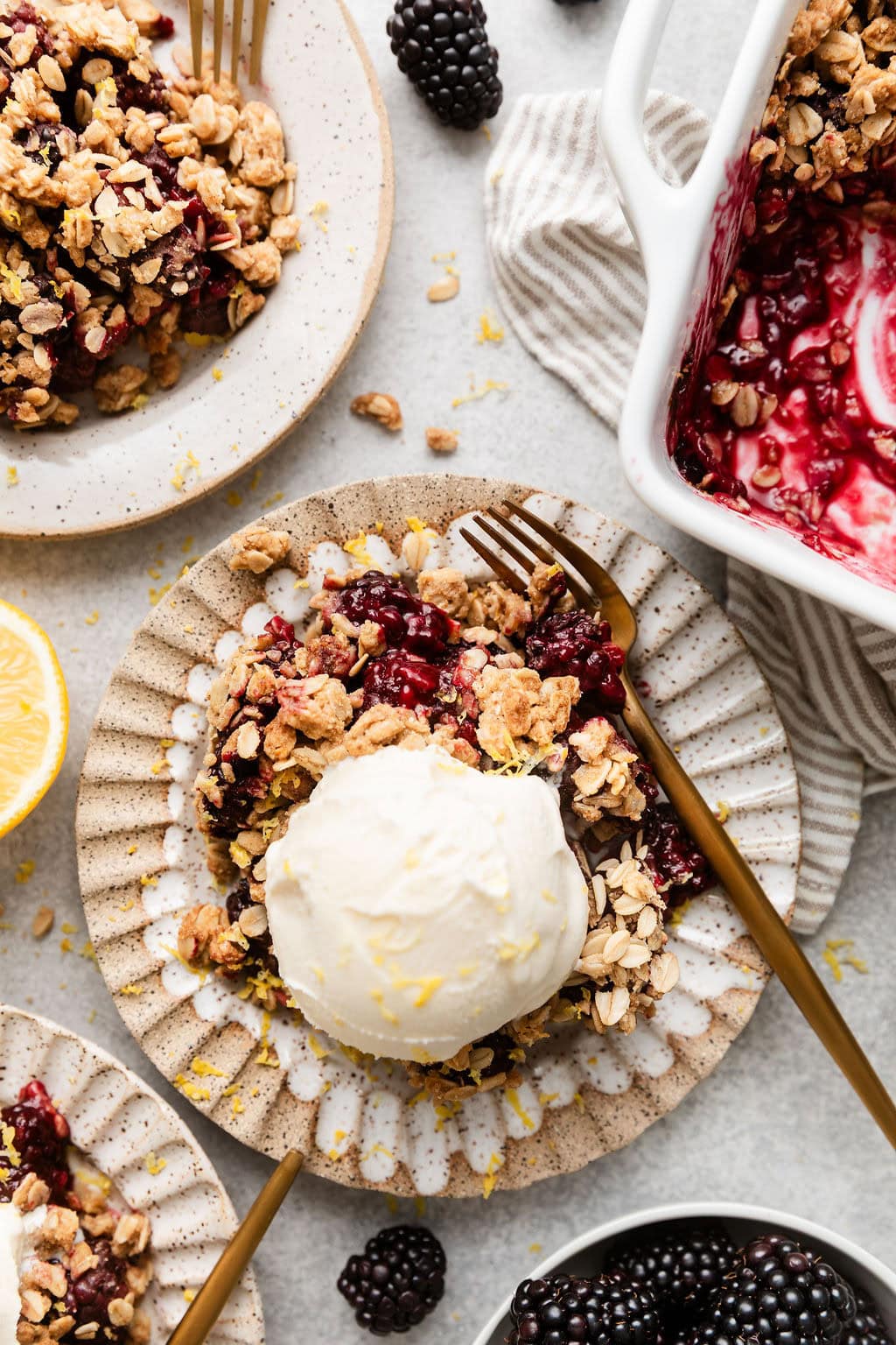 Overhead view of several plates of Blackberry Crumble topped with vanilla ice cream and sprinkled with lemon zest.