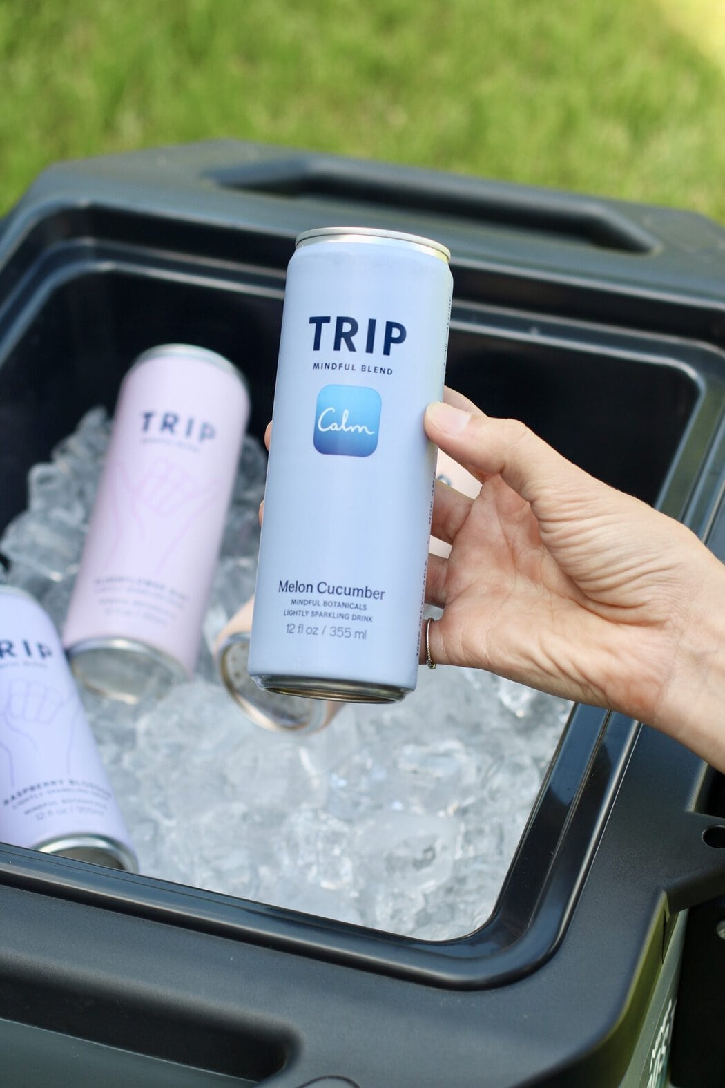 Close up view of a hand holding a canned trip mocktail over a cooler of ice.