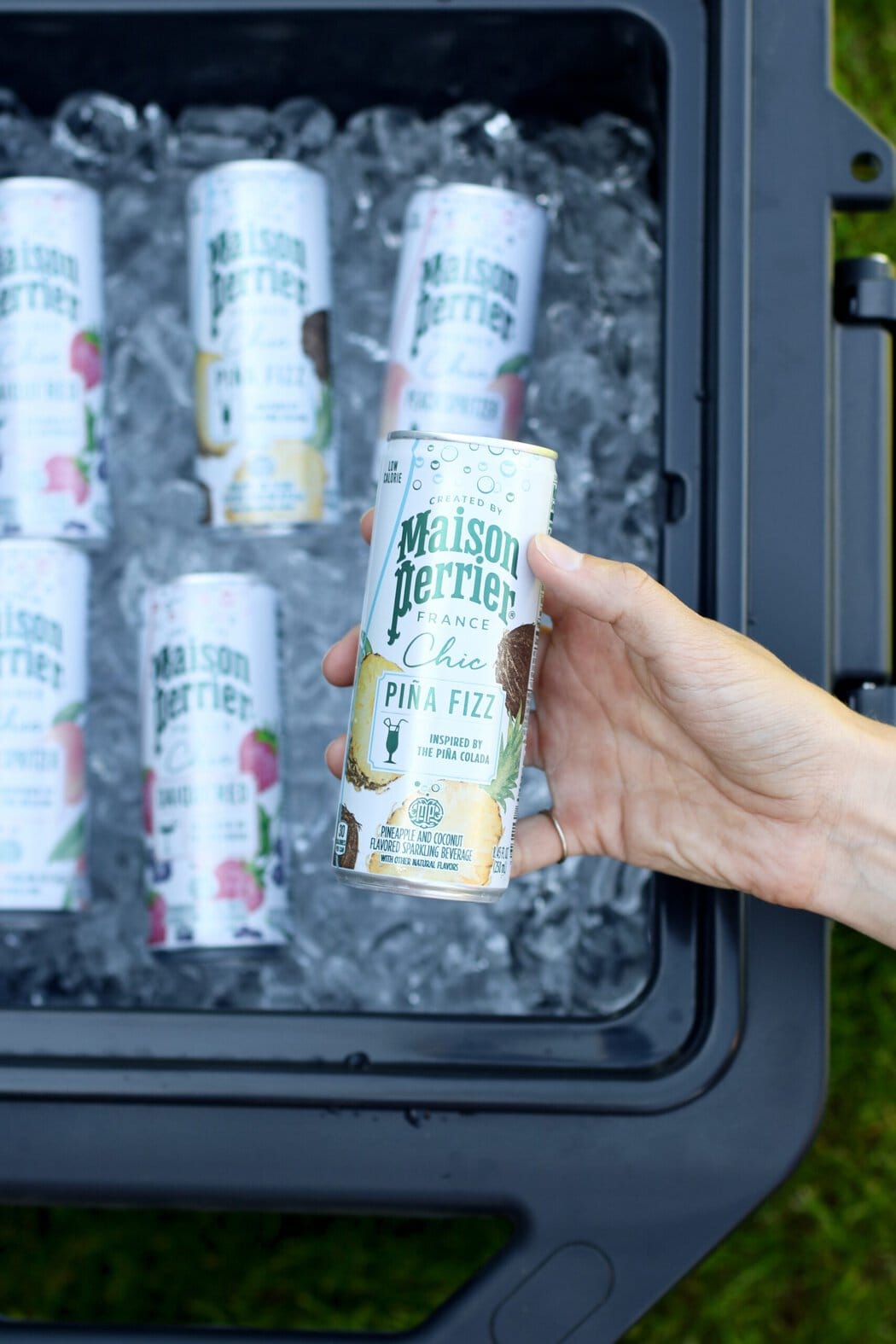Overhead view of a hand holding a canned mocktail over a cooler filled with ice and other cans.