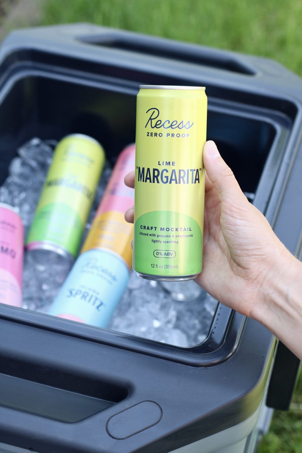 Close up view of a hand holding a canned margarita over a cooler full of ice.
