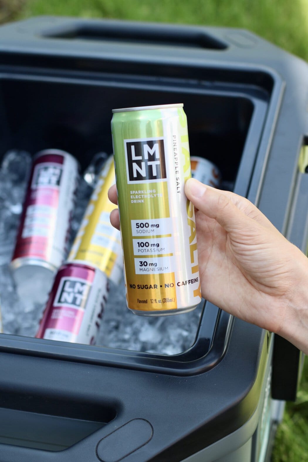 Close up view of a hand holding a canned LMNT sparkling drink over a cooler of ice.