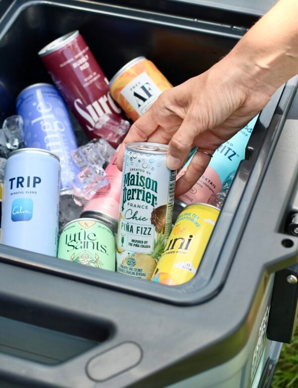 A cooler filled with canned mocktails on ice, one can being lifted from the cooler