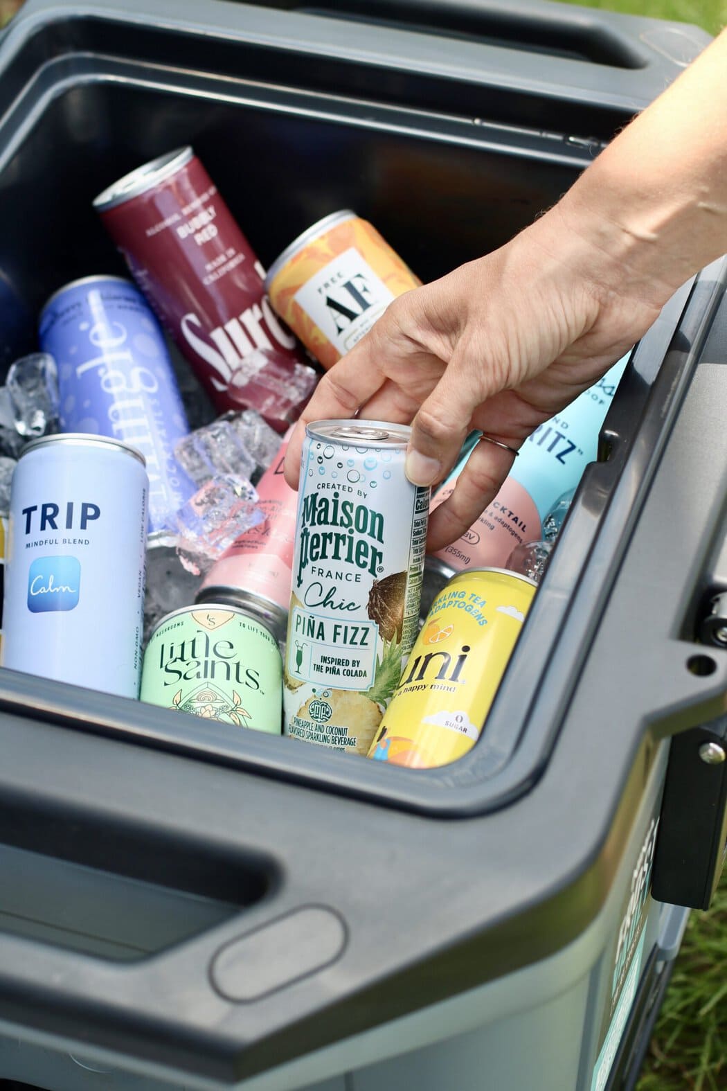 Close up view of a hand pulling out a canned mocktail from a cooler full of ice. 