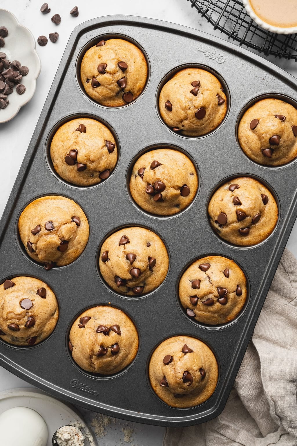 Overhead view of a muffin pan filled with freshly baked Peanut Butter Protein Muffins studded with chocolate chips.