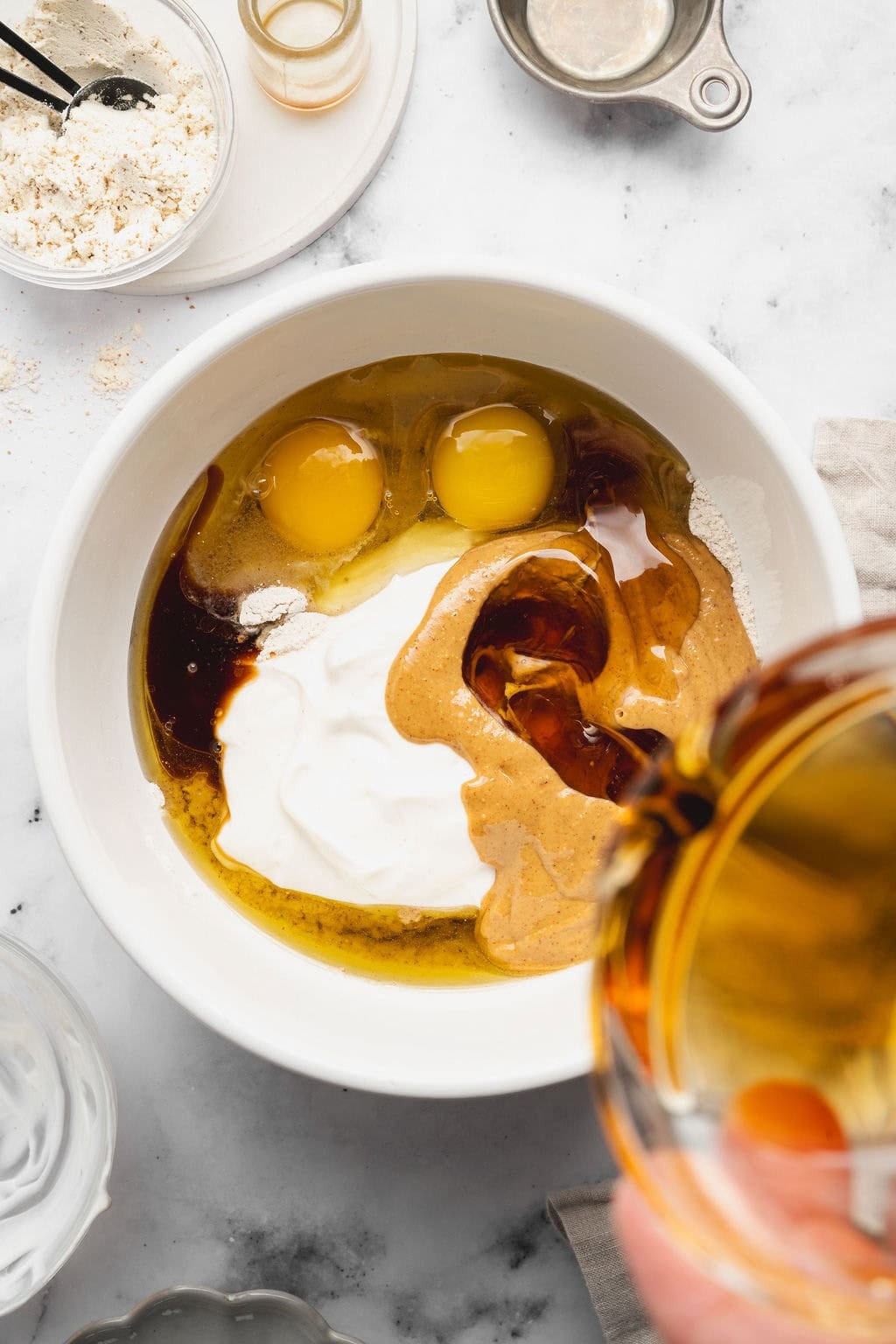 Overhead view of a bowl filled with liquid ingredients for Peanut Butter Protein Muffins including eggs and peanut butter ready to be stirred. 