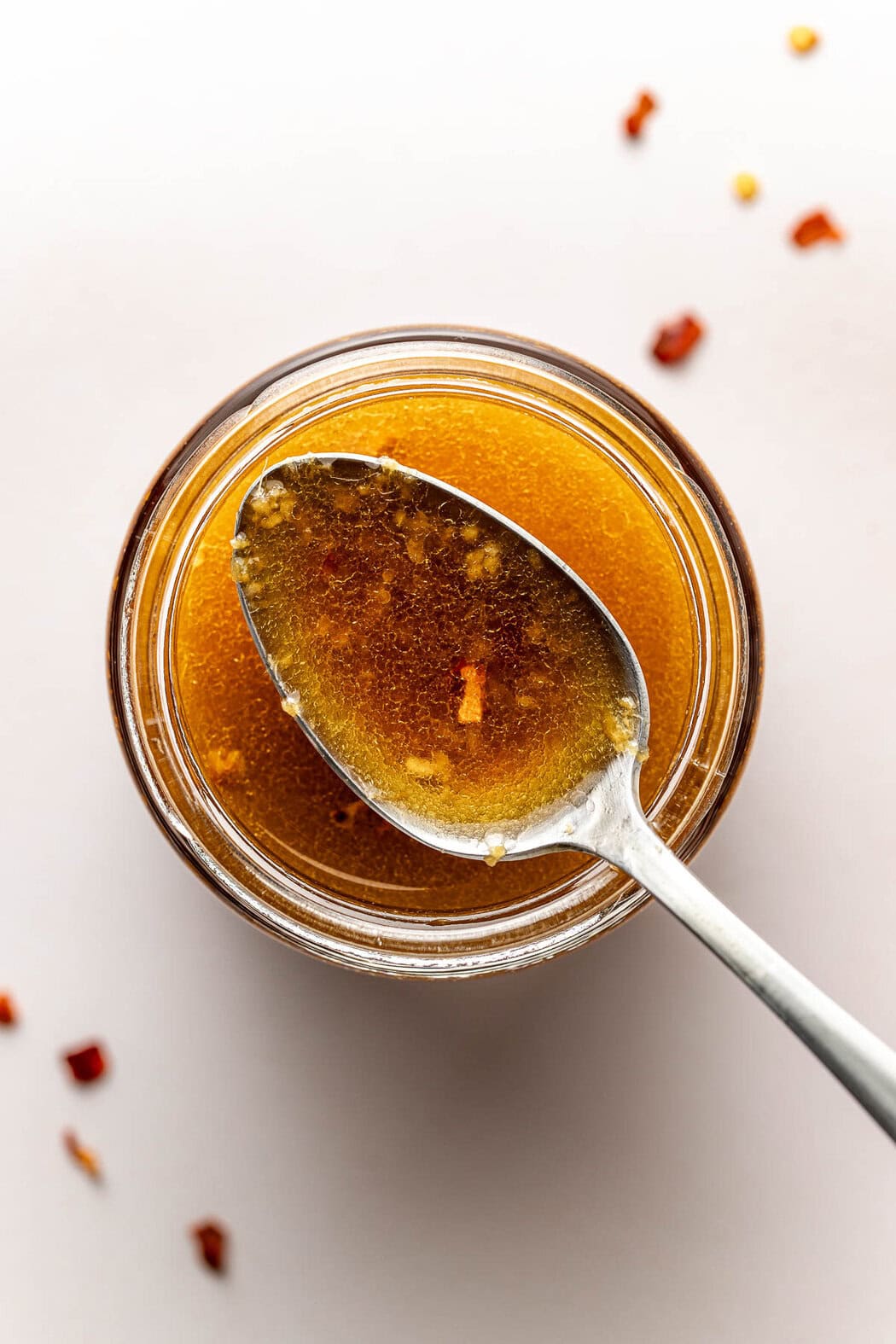Overhead view of a small glass jar of homemade dressing with a spoon showing the oily consistency.