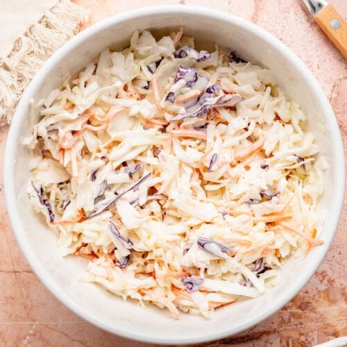 Overhead view of a white bowl filled with colorful coleslaw.