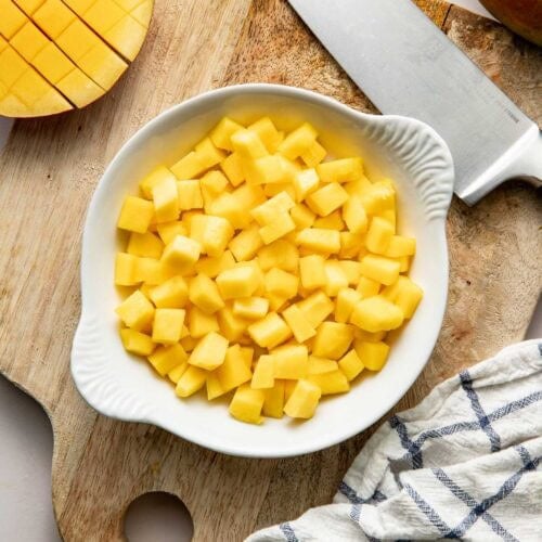 Overhead view of a bowl of freshly diced mango on a wooden cutting board.