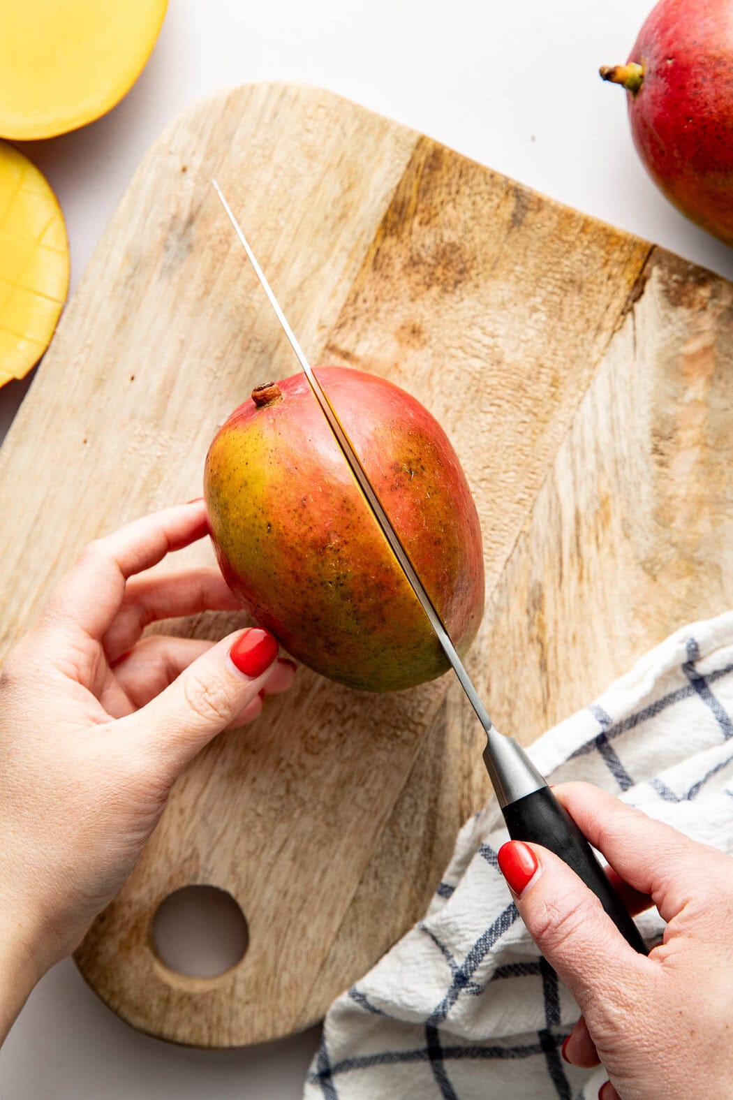 Overhead view of a mango on a wooden cutting board on its side with a knife going into the fruit.