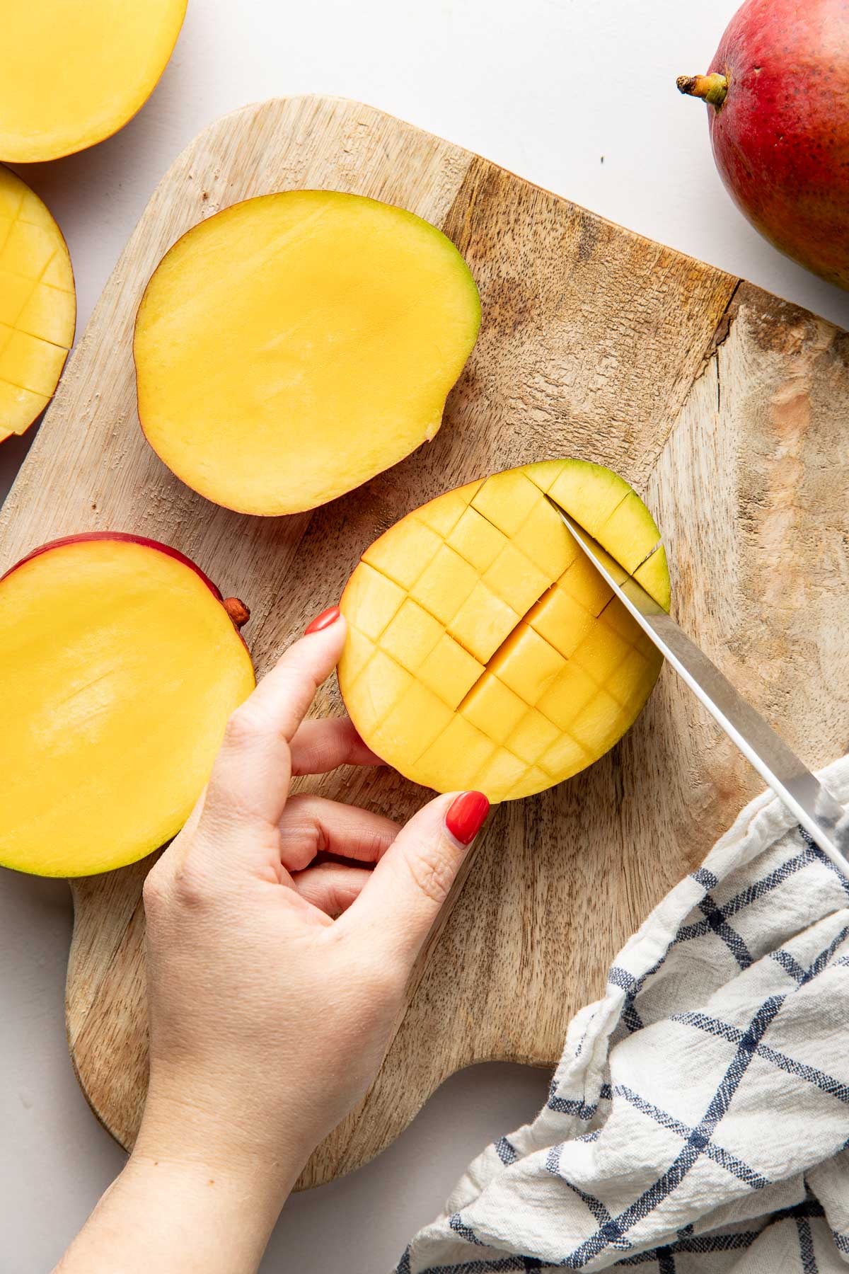 Overhead view of mangos on a wooden cutting board with a hand holding and slicing. 