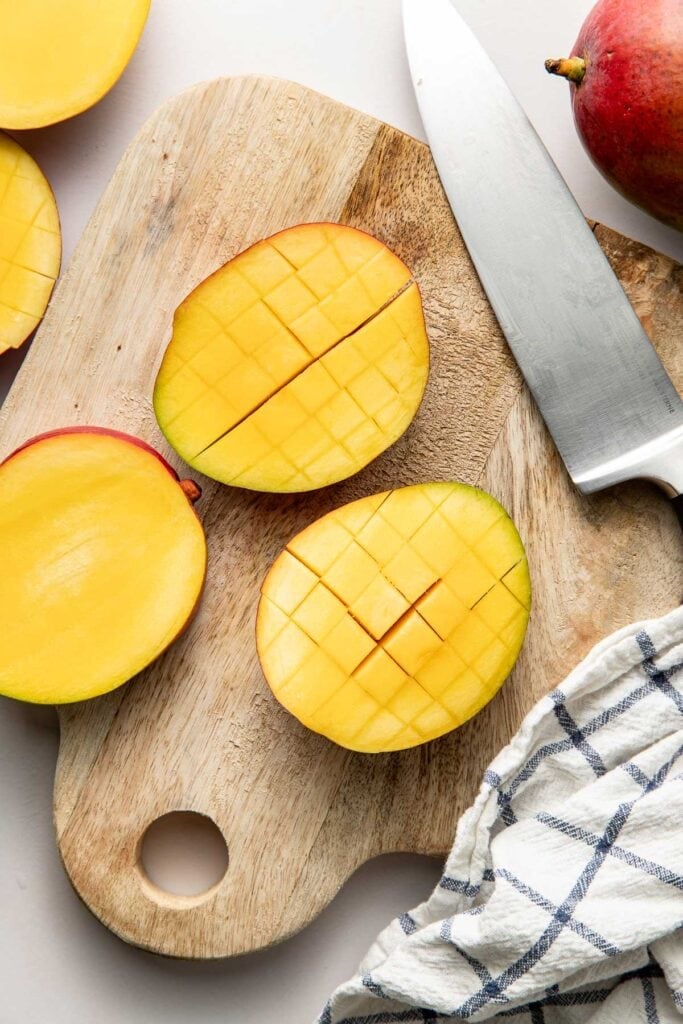 Overhead view of a mango on a cutting board scored into small square shaped pieces. 