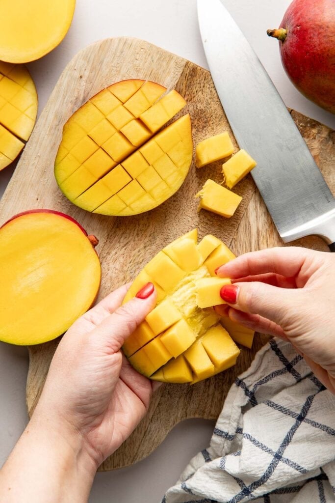 Overhead view of hands gently peeling away small squares of mango from the peeling. 