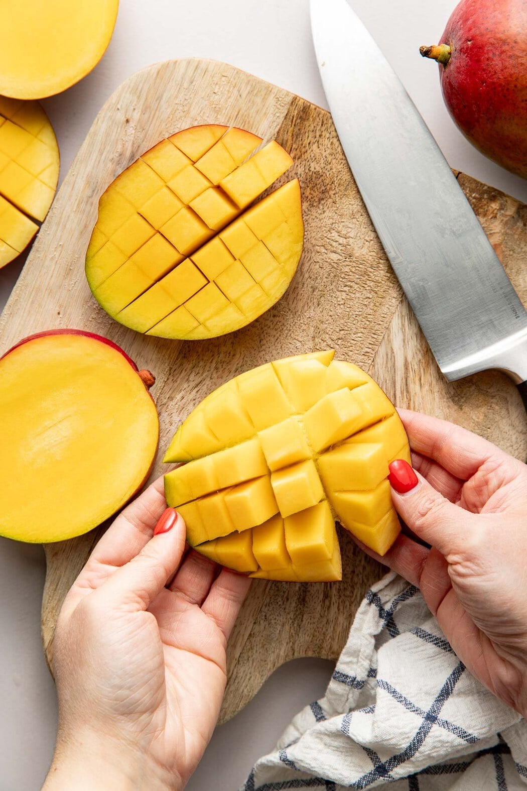 Overhead view of sliced mangos on a wooden cutting board with a knife on the side.