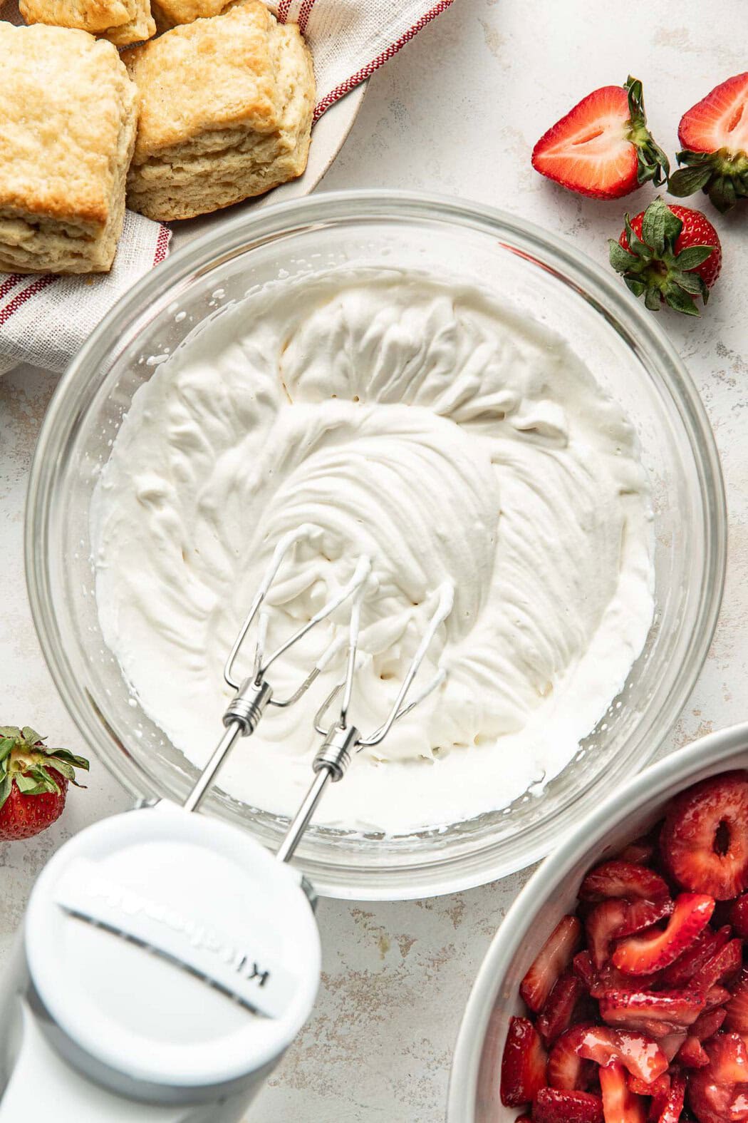 Overhead view of a glass bowl filled with freshly whipped cream with an electric mixer on the side of the bowl.