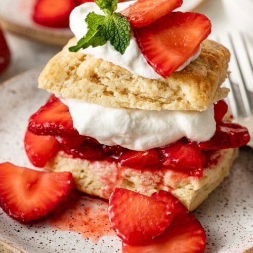 Close up view of a layered Strawberry Shortcake topped with whipped cream and garnished with fresh mint leaves.