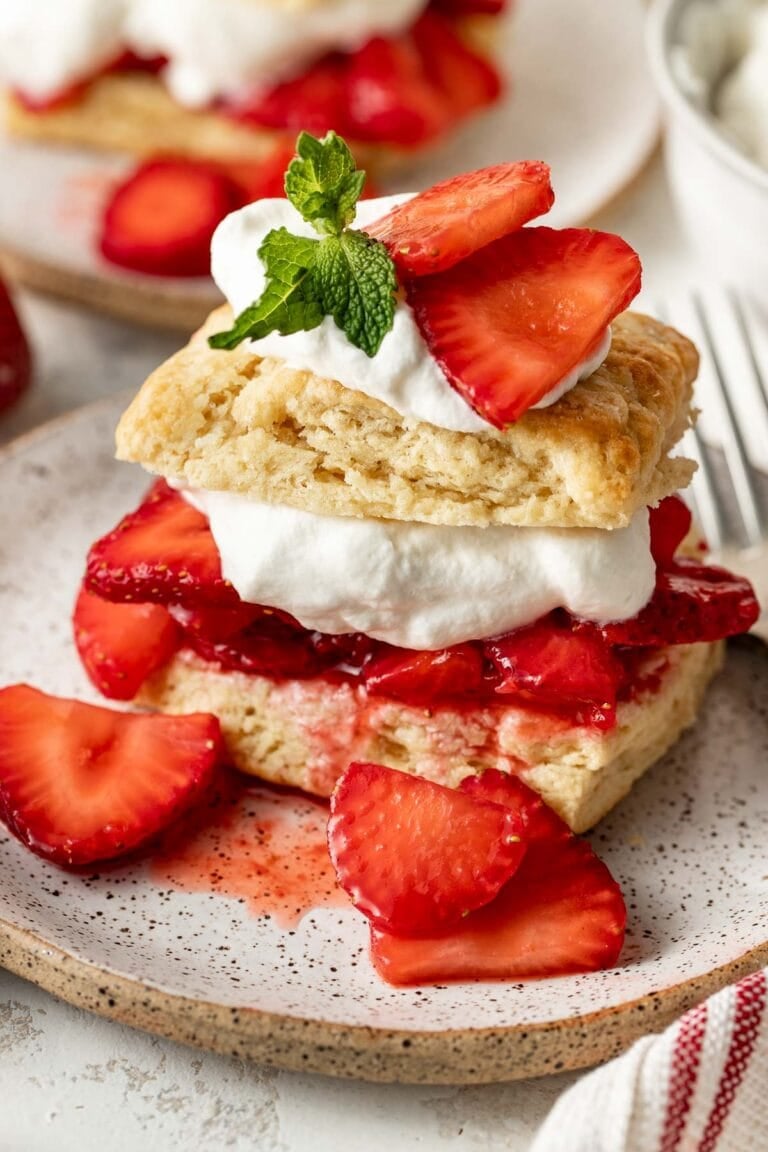 Close up view of a piece of strawberry shortcake topped with macerated strawberries and whipped cream.