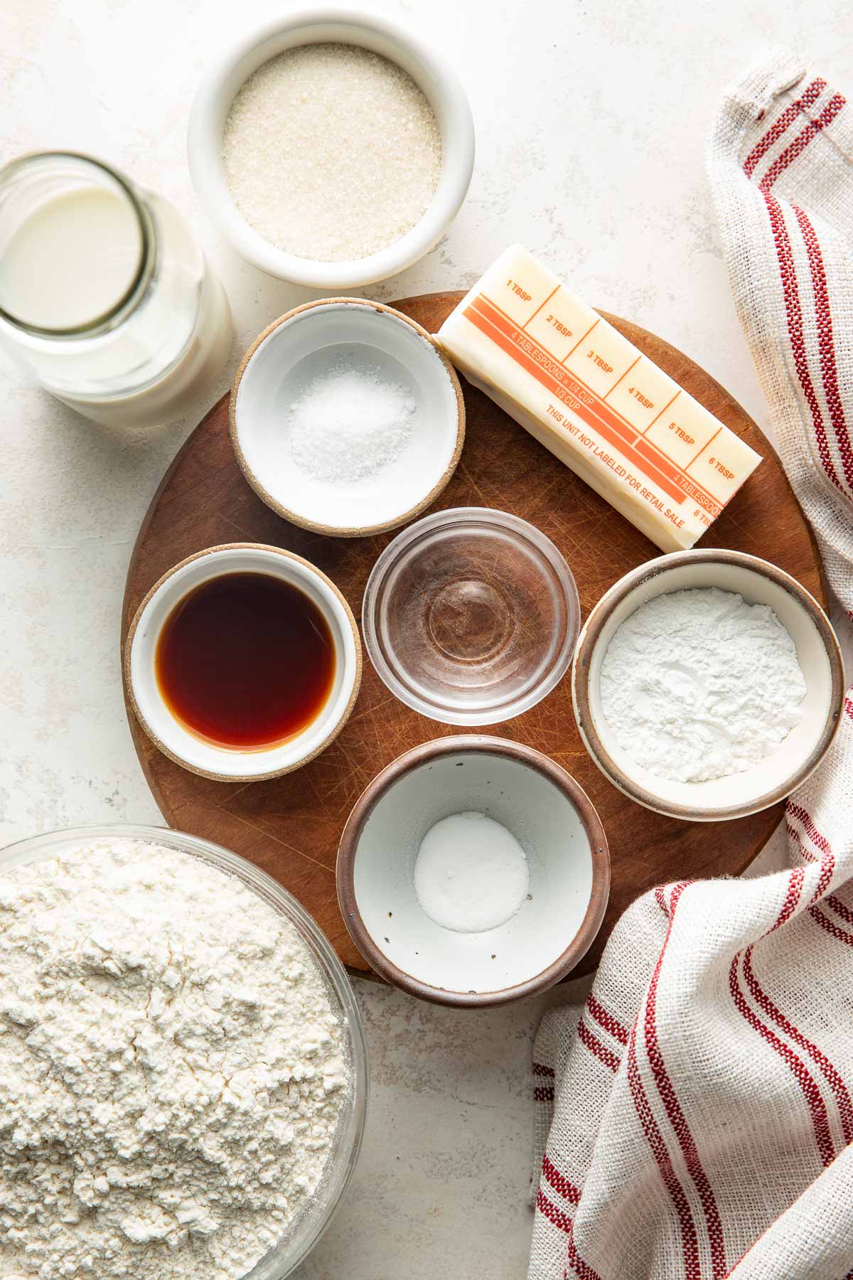 Overhead view of a variety of ingredients for Sweet Cream Biscuits arranged on a wooden cutting board.