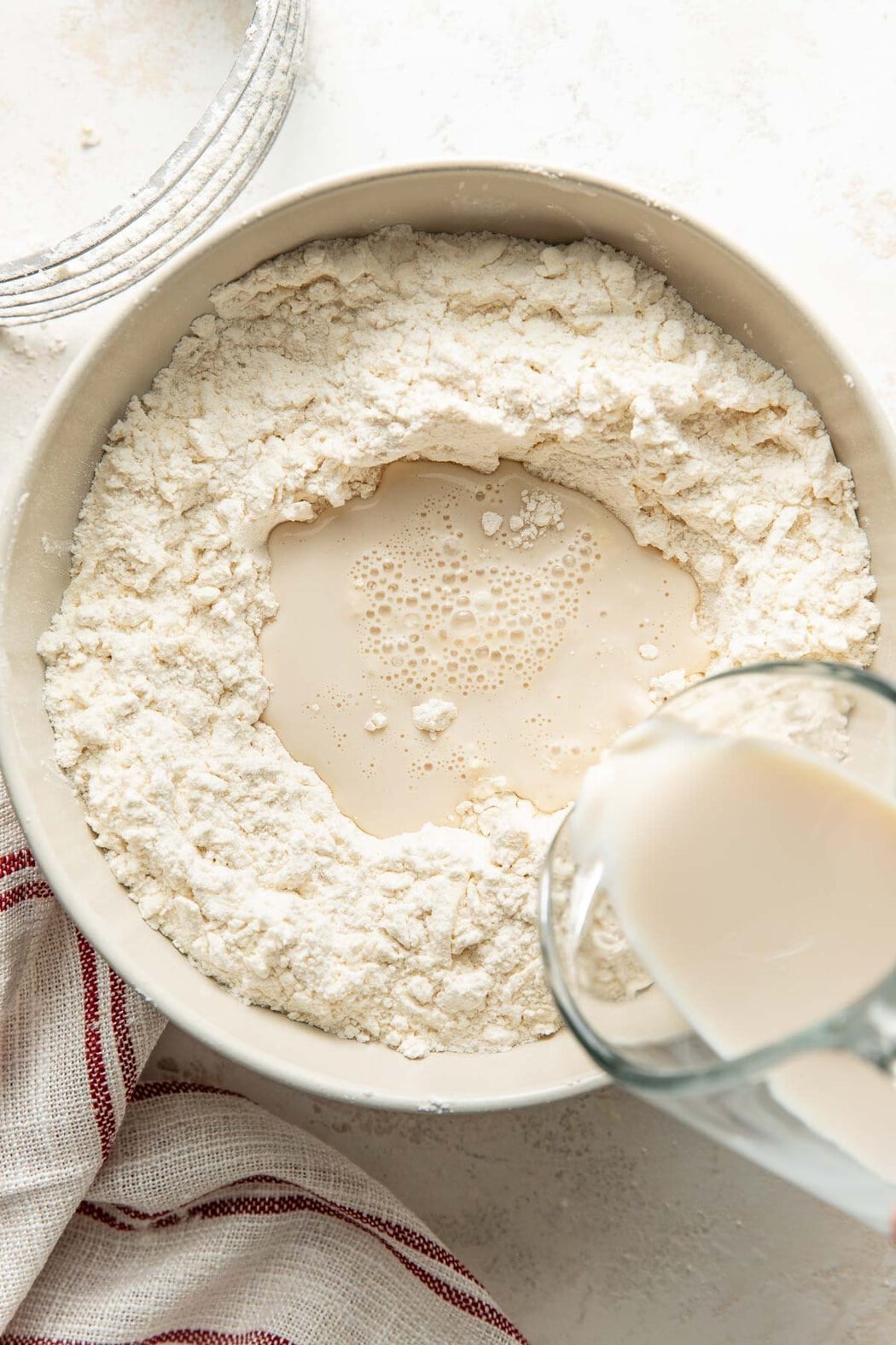 Overhead view of a bowl of flour with cream being poured on top.